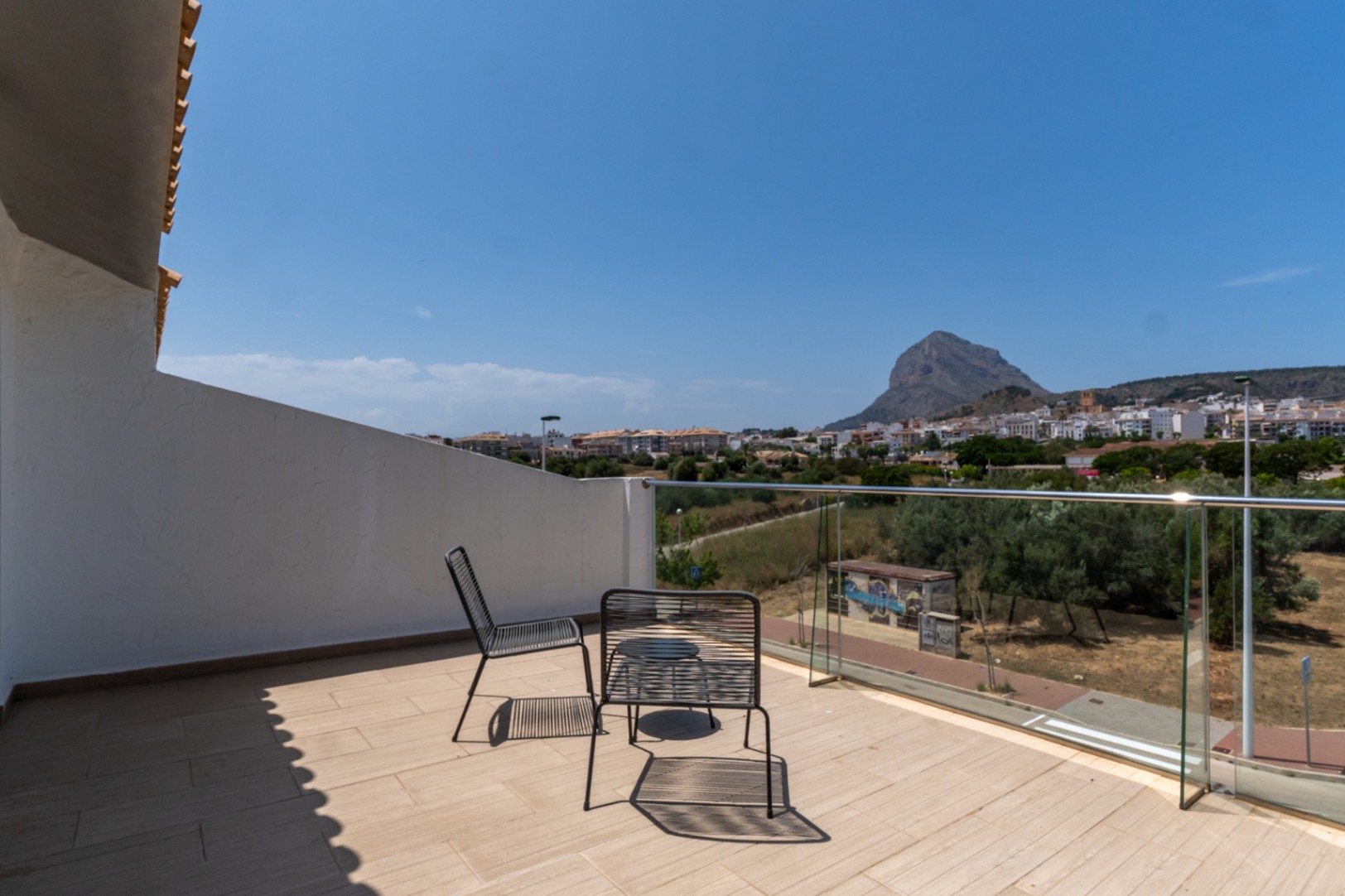 Bovenste terras met glazen balustrade en panoramisch uitzicht op de Montgó en Jávea. Voorzien van modern metalen meubilair en een lichte tegelvloer.