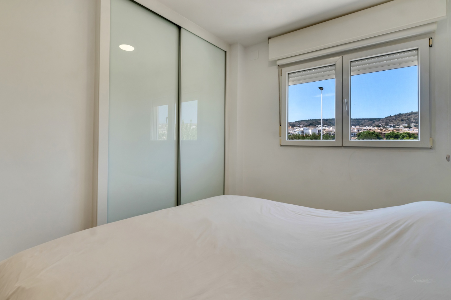 Lichte slaapkamer met een inbouwkast met matglazen schuifdeuren en een raam met dubbele beglazing dat uitzicht biedt op de heuvels van Jávea.