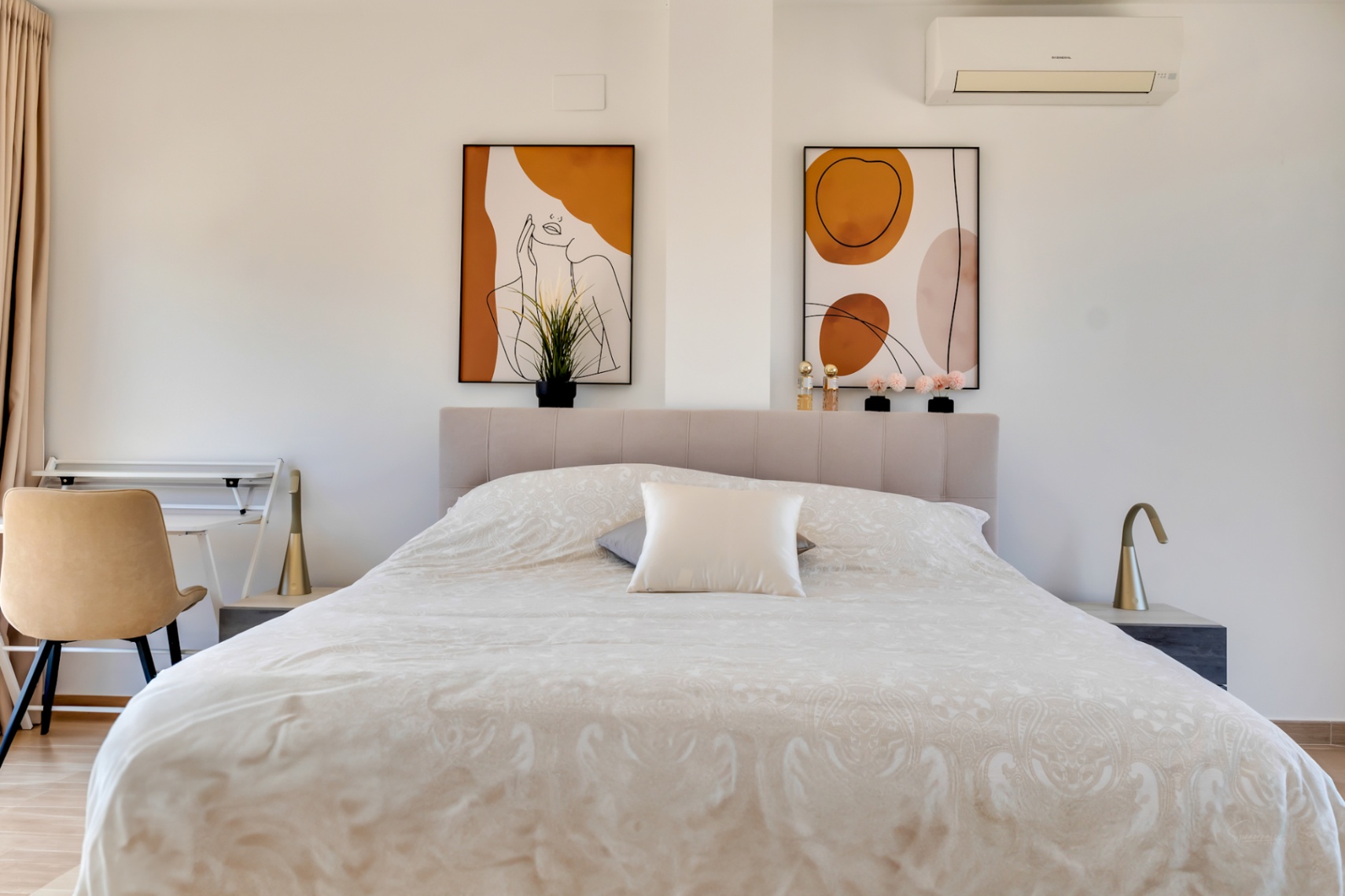 Lichte slaapkamer met gestoffeerd hoofdbord, abstracte kunst in aardetinten en een compacte werkplek. Voorzien van airconditioning en minimalistische designlampen.