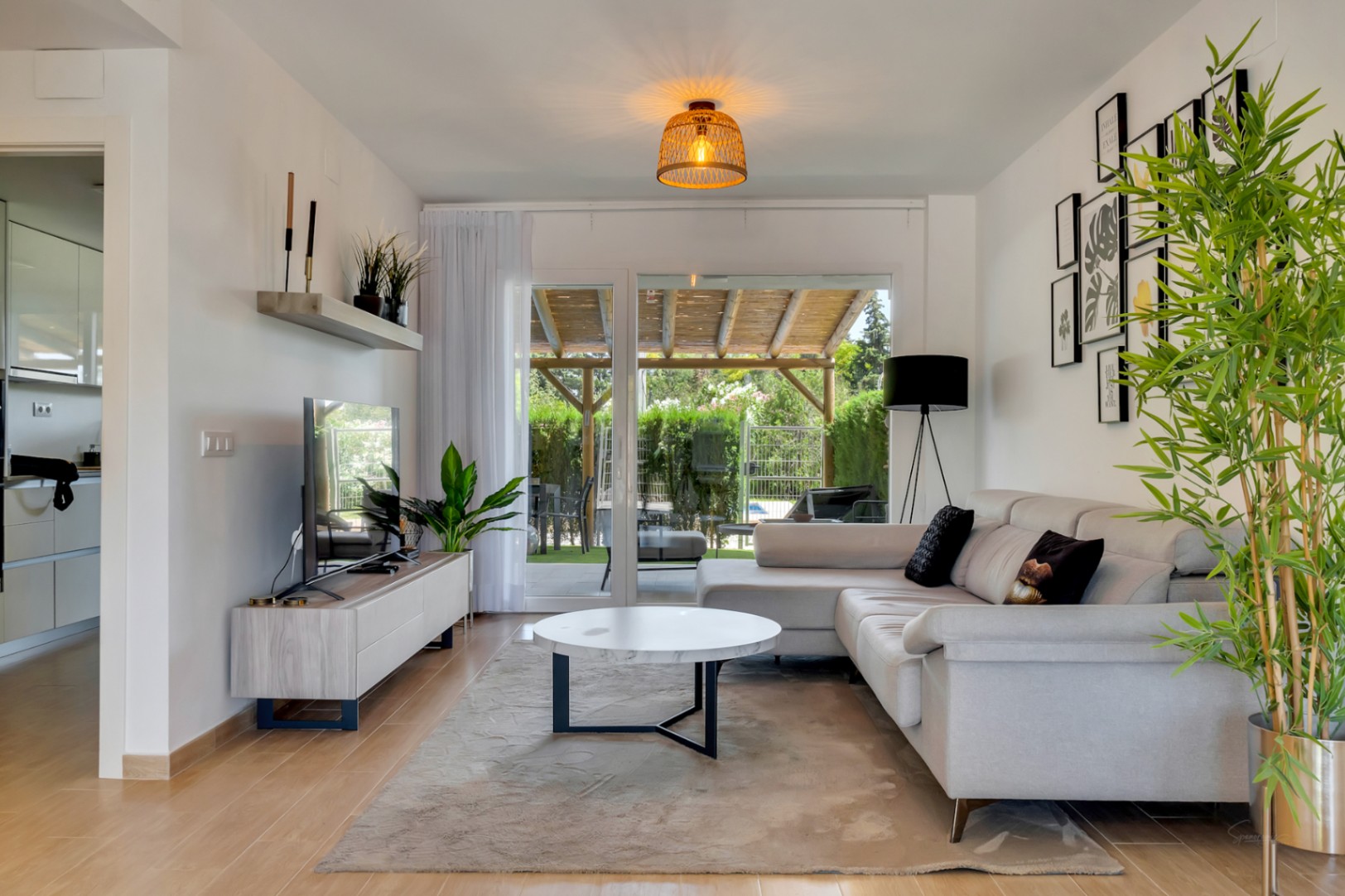Lichte woonkamer met hoekbank, marmeren salontafel en grote schuifpui naar de privépatiomet houten pergola, wat zorgt voor veel natuurlijk licht en direct contact met buiten.