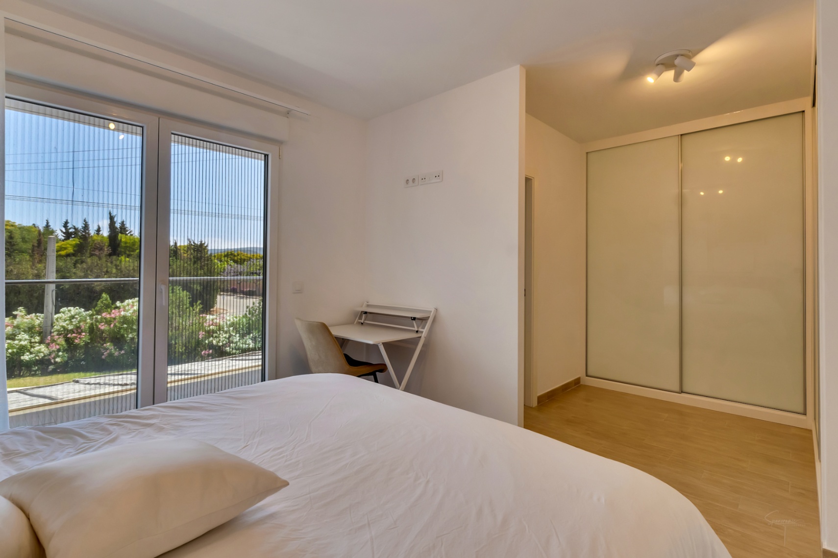Lichtrijke slaapkamer met witte inbouwkast, een compacte werkplek en directe toegang tot het balkon via een glazen schuifdeur met geïntegreerd horrengaas.