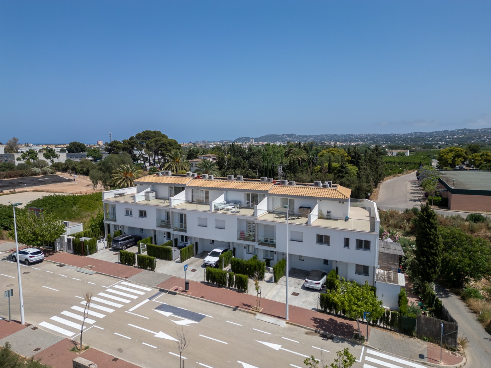 Luchtfoto van het moderne geschakelde woningcomplex met privéparkeerplaatsen aan de voorzijde, witte gevels en ruime dakterrassen met glazen balustrades.