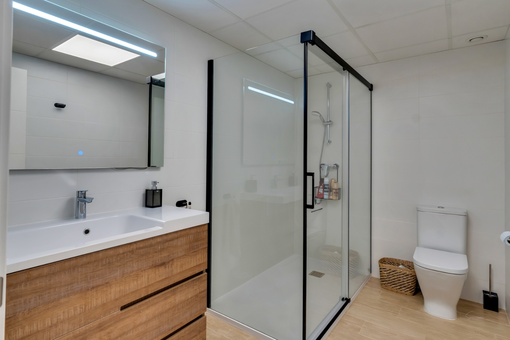 Moderne badkamer met houten wastafelmeubel, LED-spiegel en inloopdouche met zwart profiel, afgewerkt met een eigentijdse vloer in houtlook.