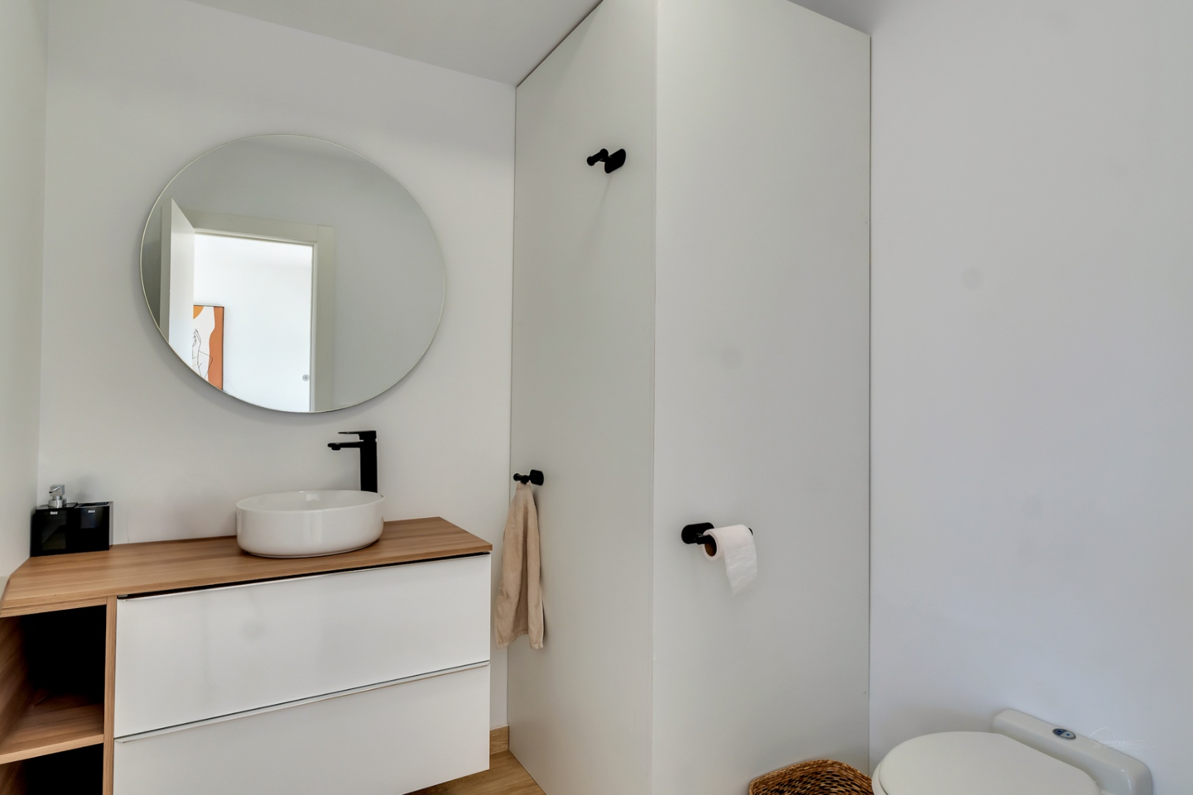 Moderne toiletruimte met een opzetwastafel op een houten blad, matzwarte kranen en een ronde spiegel. Het witte zwevende meubel biedt een strakke, eigentijdse uitstraling.