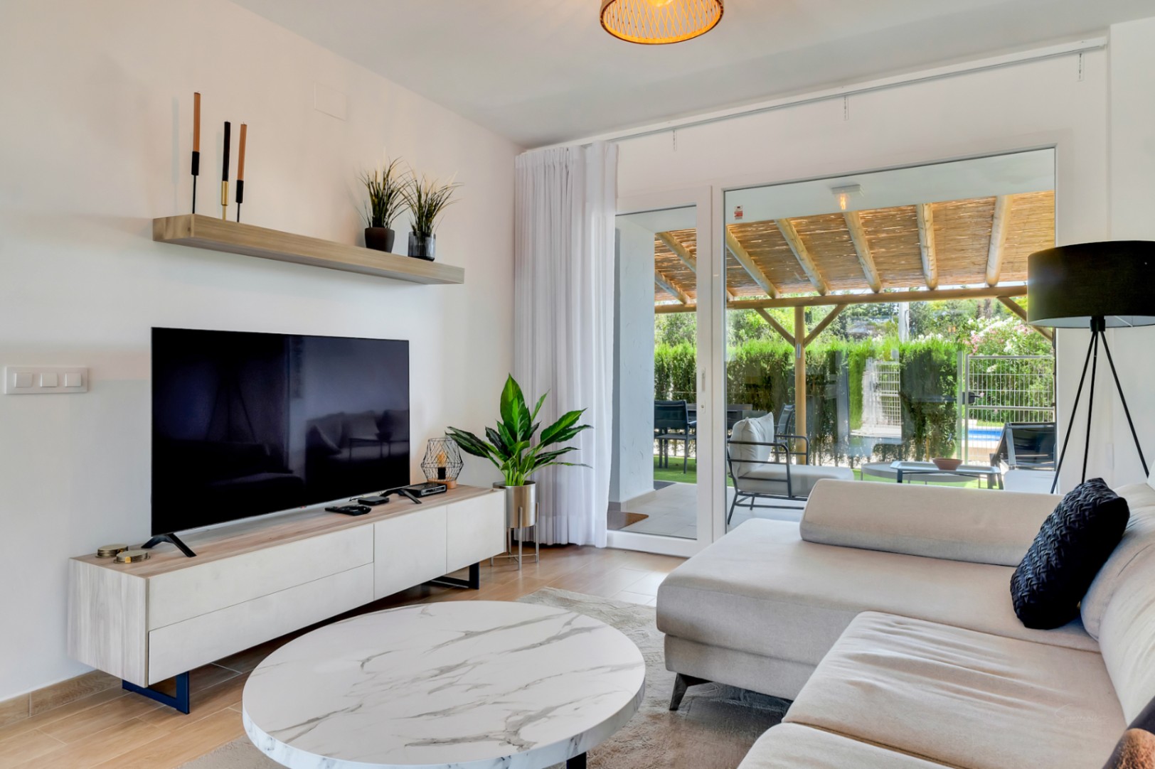 Open woonkamer met modern meubilair en grote glazen schuifdeuren die directe toegang bieden tot de privépatiomet houten pergola.