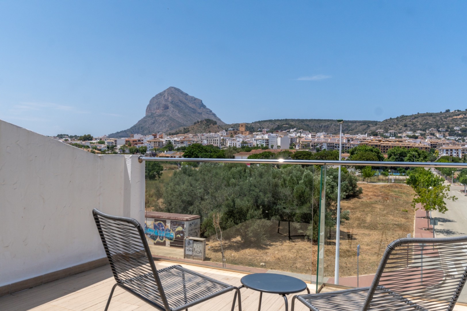 Privéterras op de bovenste verdieping met panoramisch uitzicht op de Montgó en Jávea, voorzien van modern meubilair en een glazen balustrade.