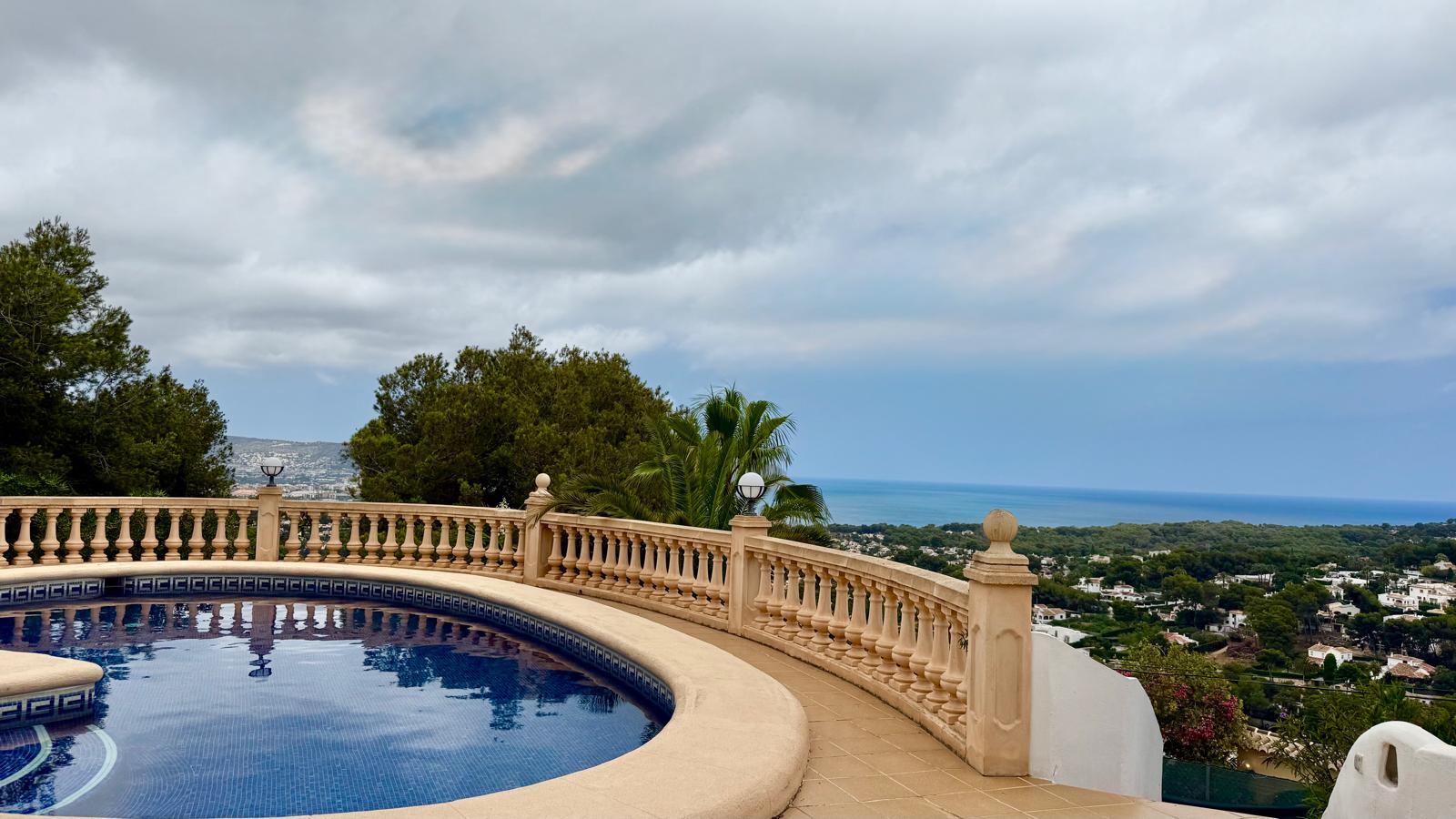 Cirkelvormig zwembad met blauwe mozaïektegels en een klassieke stenen balustrade, met panoramisch uitzicht op de Middellandse Zee en de kust van Jávea.