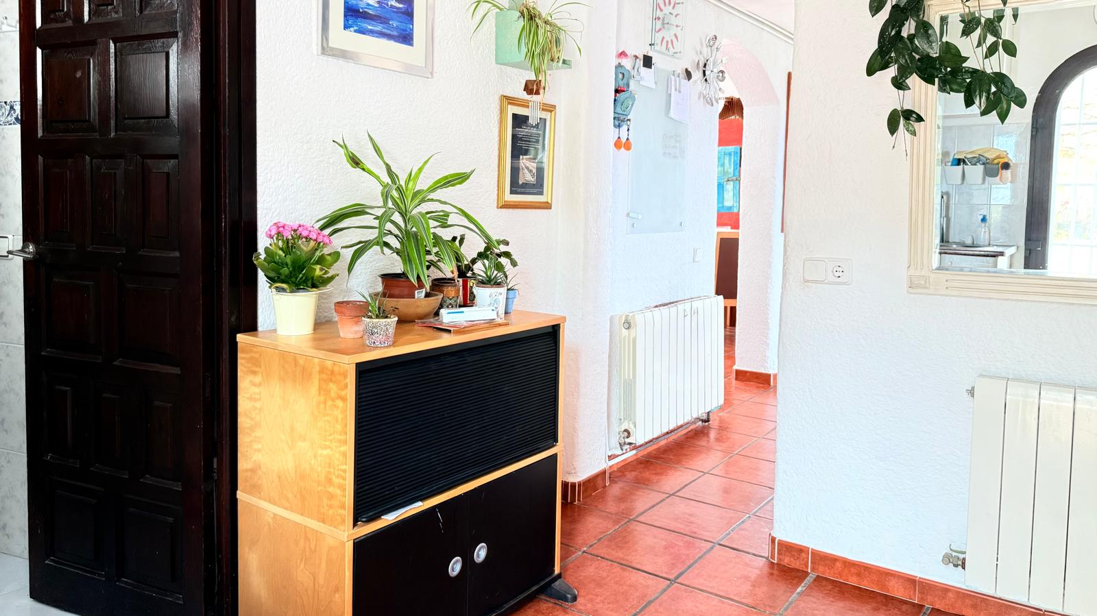 Entreehal met traditionele terracotta vloertegels, witte muren met textuur en een radiator. Een donkere houten deur en een boog leiden naar de overige woonruimtes.