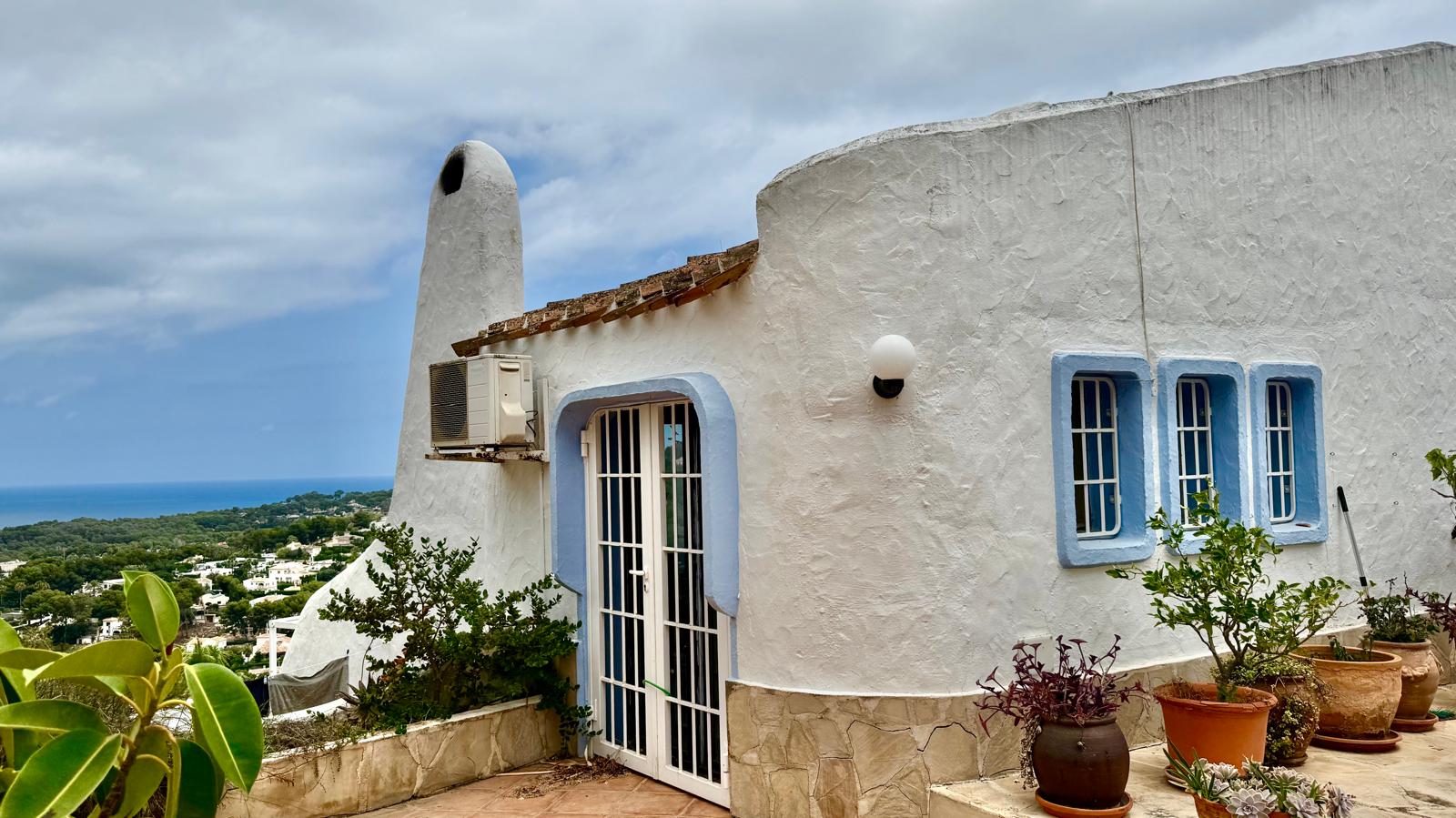 Exterieur in Ibiza-stijl met ronde witte muren en blauwe kozijnen. De sculpturale schoorsteen en terracotta potten sieren het terras met uitzicht op de Middellandse Zee.