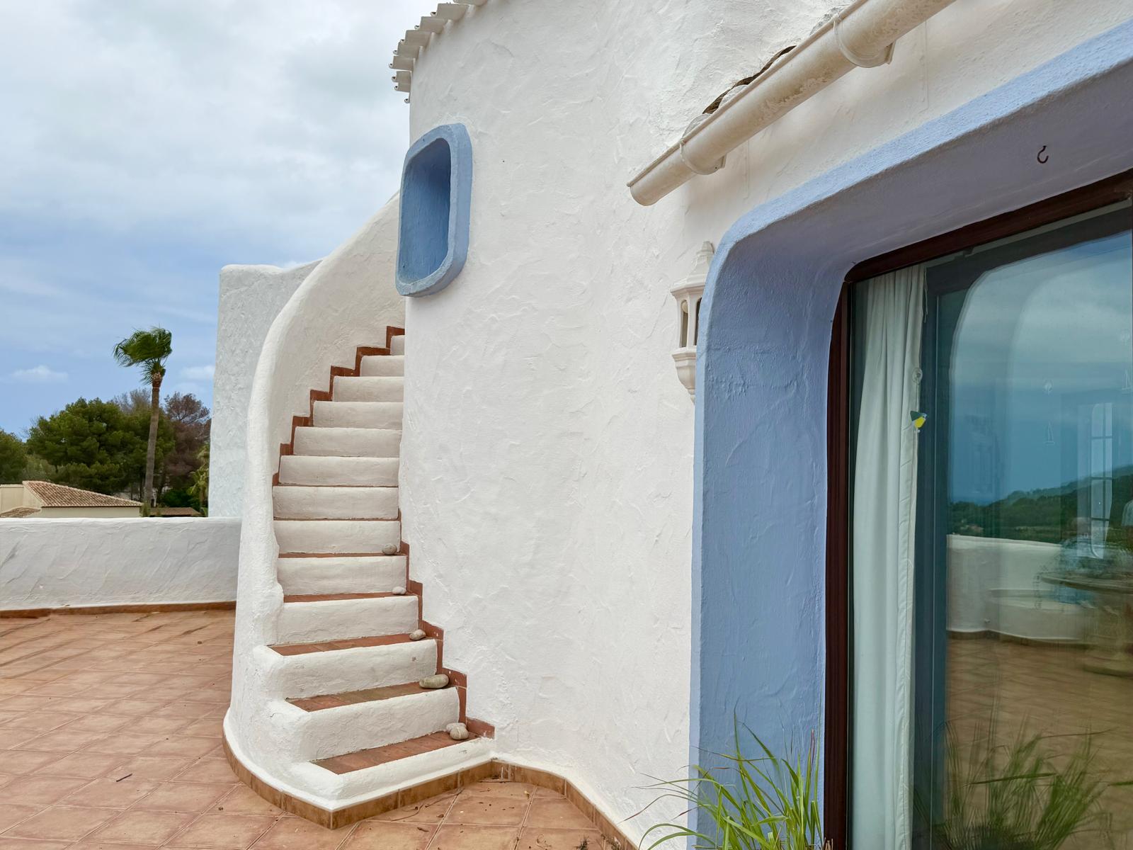 Exterieur in Ibizastijl met een gebogen witte trap, terracotta treden en blauw omlijste accenten grenzend aan het betegelde terras.