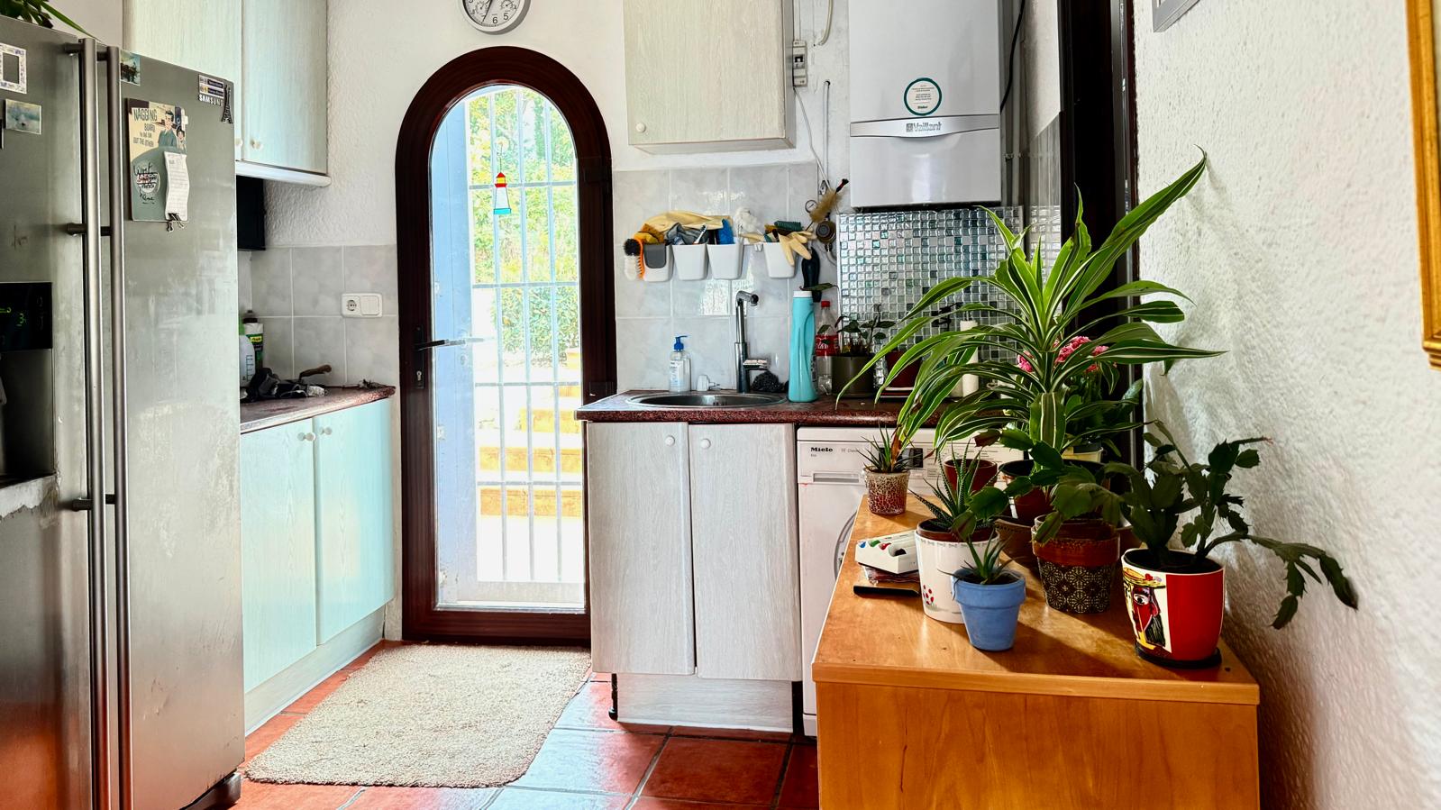 Functionele keuken met een gewelfde glazen deur, granieten werkbladen en terracotta vloer. Voorzien van witte kasten, een wasruimte en veel natuurlijk licht.