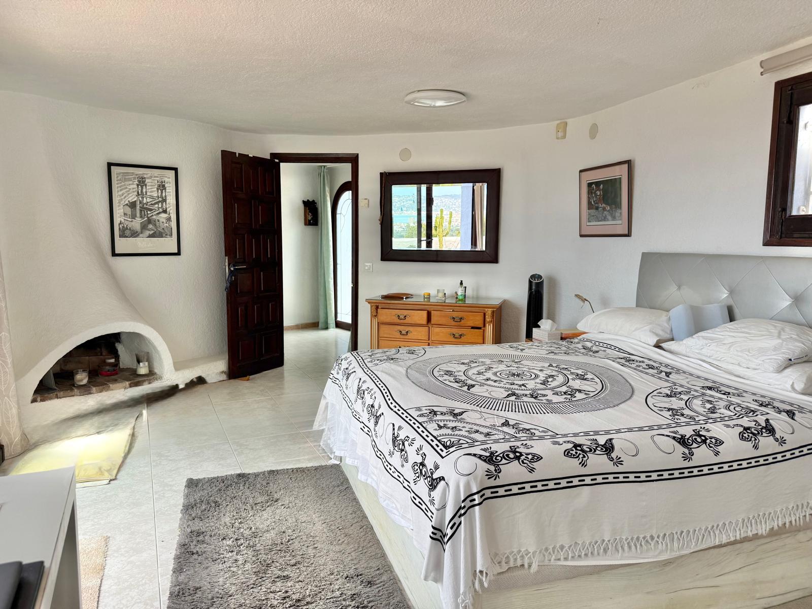 Hoofdslaapkamer in Ibiza-stijl met een ingebouwde hoekhaard, witte muren met textuur en lichte tegelvloeren die zorgen voor een heldere uitstraling.