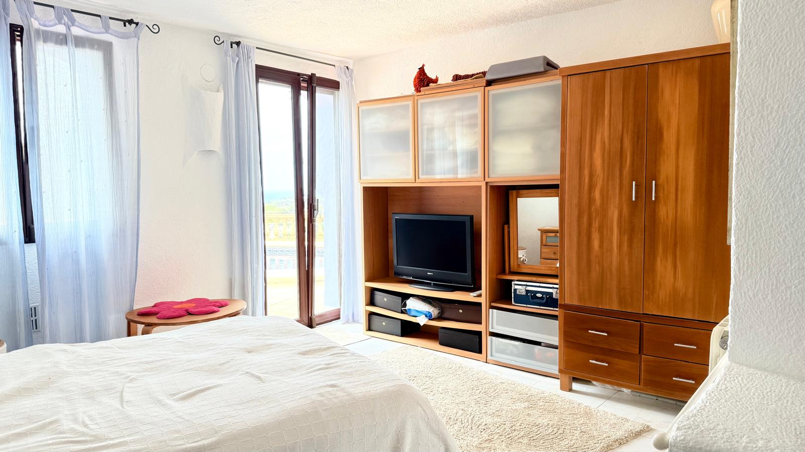 Lichte slaapkamer met houten kastenwand inclusief tv-meubel en directe toegang tot het terras met uitzicht op de omgeving.
