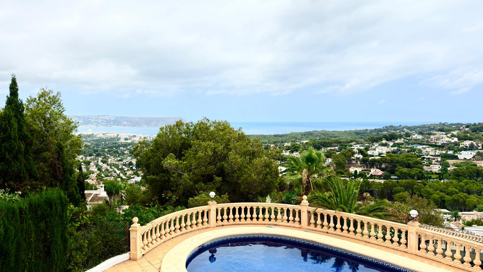 Panoramisch uitzicht op de Middellandse Zee en de baai van Jávea vanaf het bovenste terras, met een klassieke stenen balustrade boven het zwembad.