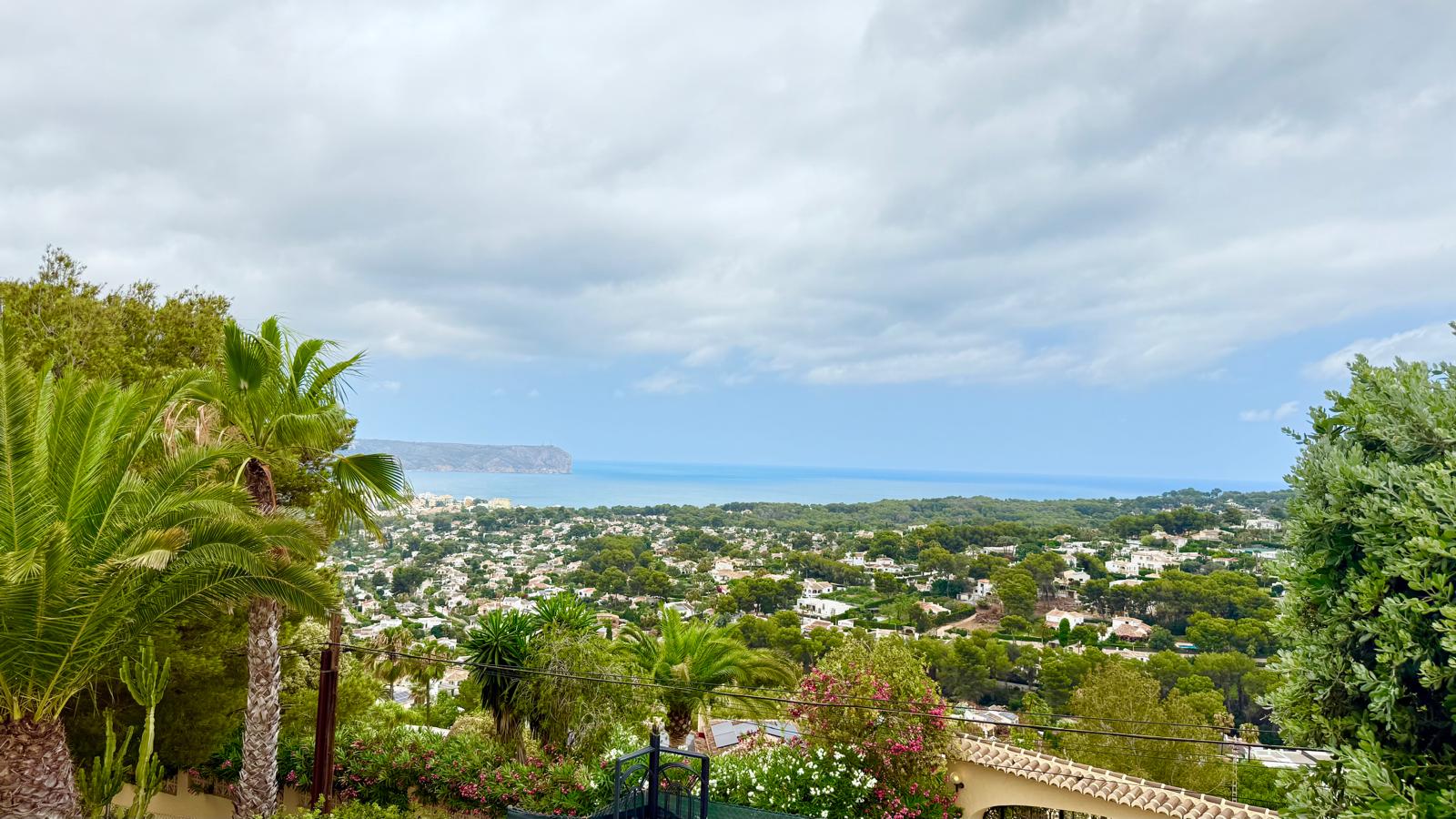 Panoramisch uitzicht vanaf het pand over de baai van Jávea en de Middellandse Zee, omlijst door volgroeide tuinbeplanting en de kaap van San Antonio.