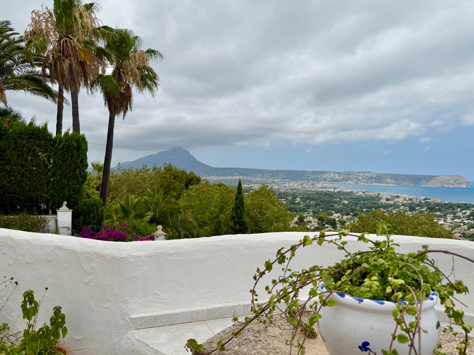 Panoramisch uitzicht vanaf het terras over de baai van Jávea en de Montgó, omlijst door mediterrane beplanting en witte muren in Ibizastijl.