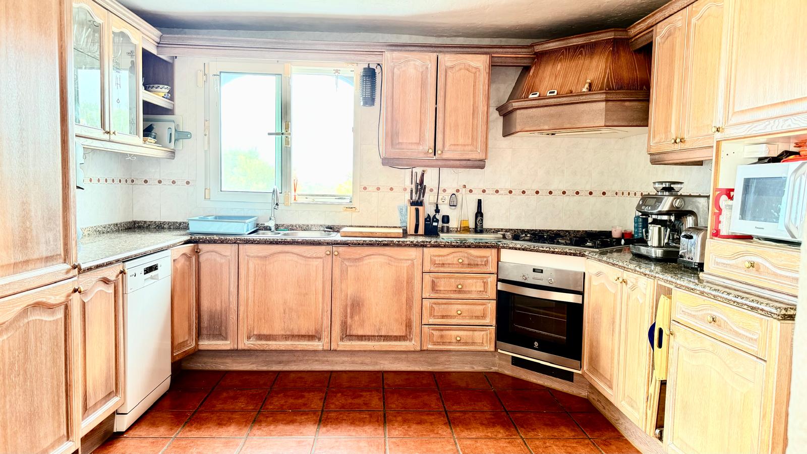 Traditionele keuken met eikenhouten meubels, granieten werkbladen, een terracotta vloer en een raam dat natuurlijk licht boven het aanrecht biedt.