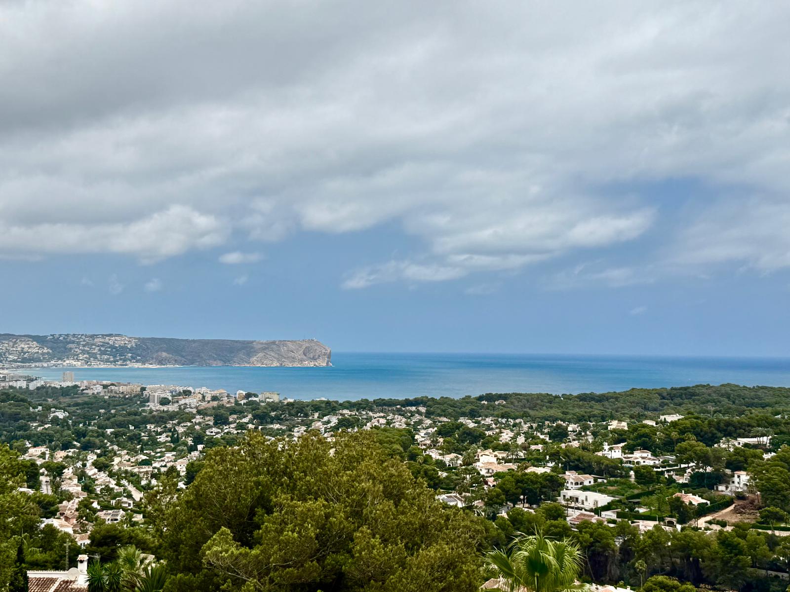 Verhoogd panoramisch uitzicht over de baai van Jávea en Cap de Sant Antoni, met de Middellandse Zee en de groene residentiële omgeving.