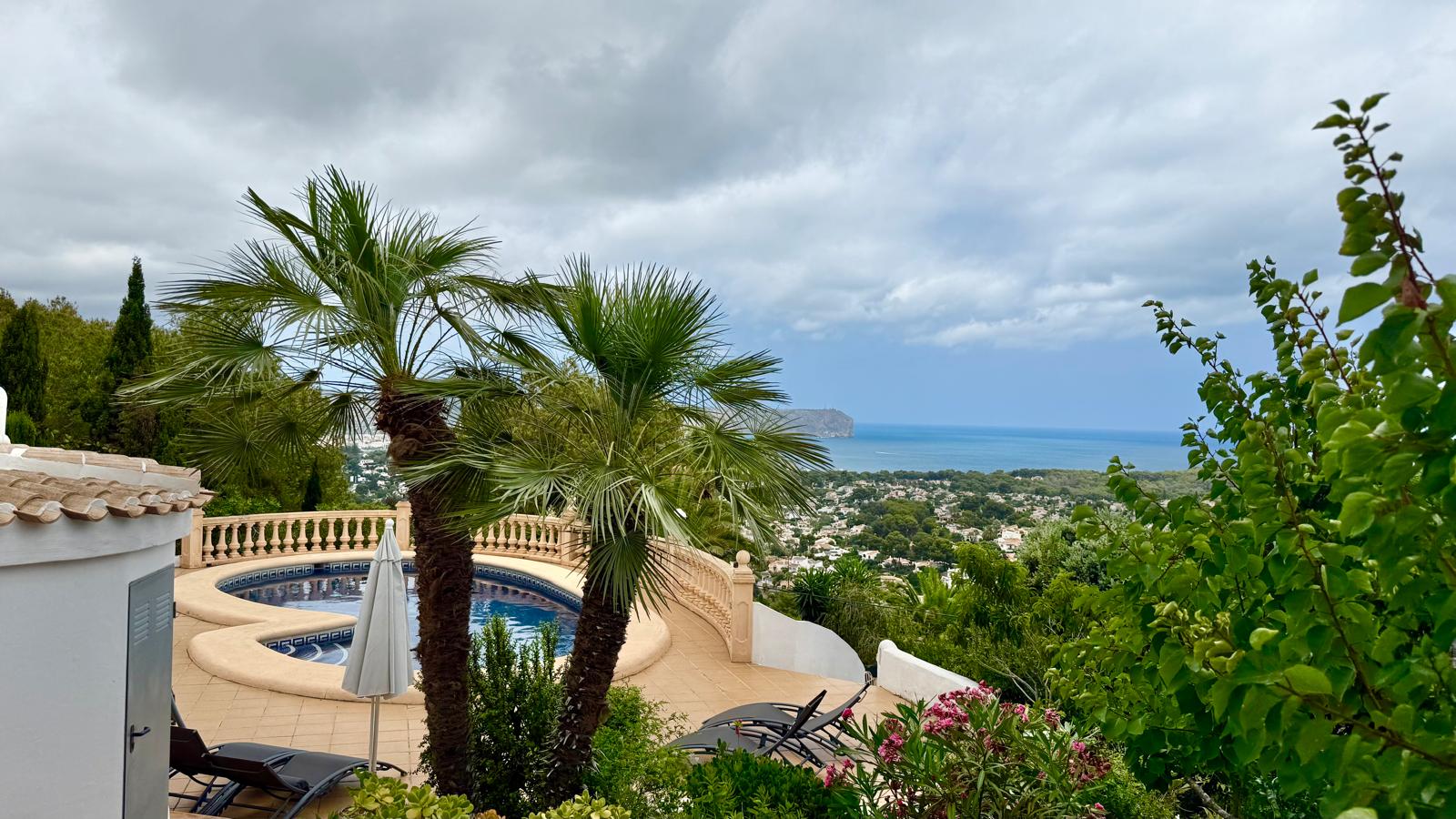 Verhoogd uitzicht op het niervormige zwembad en de mediterrane tuin met panoramisch zicht over de baai van Jávea en de omliggende kustlijn.