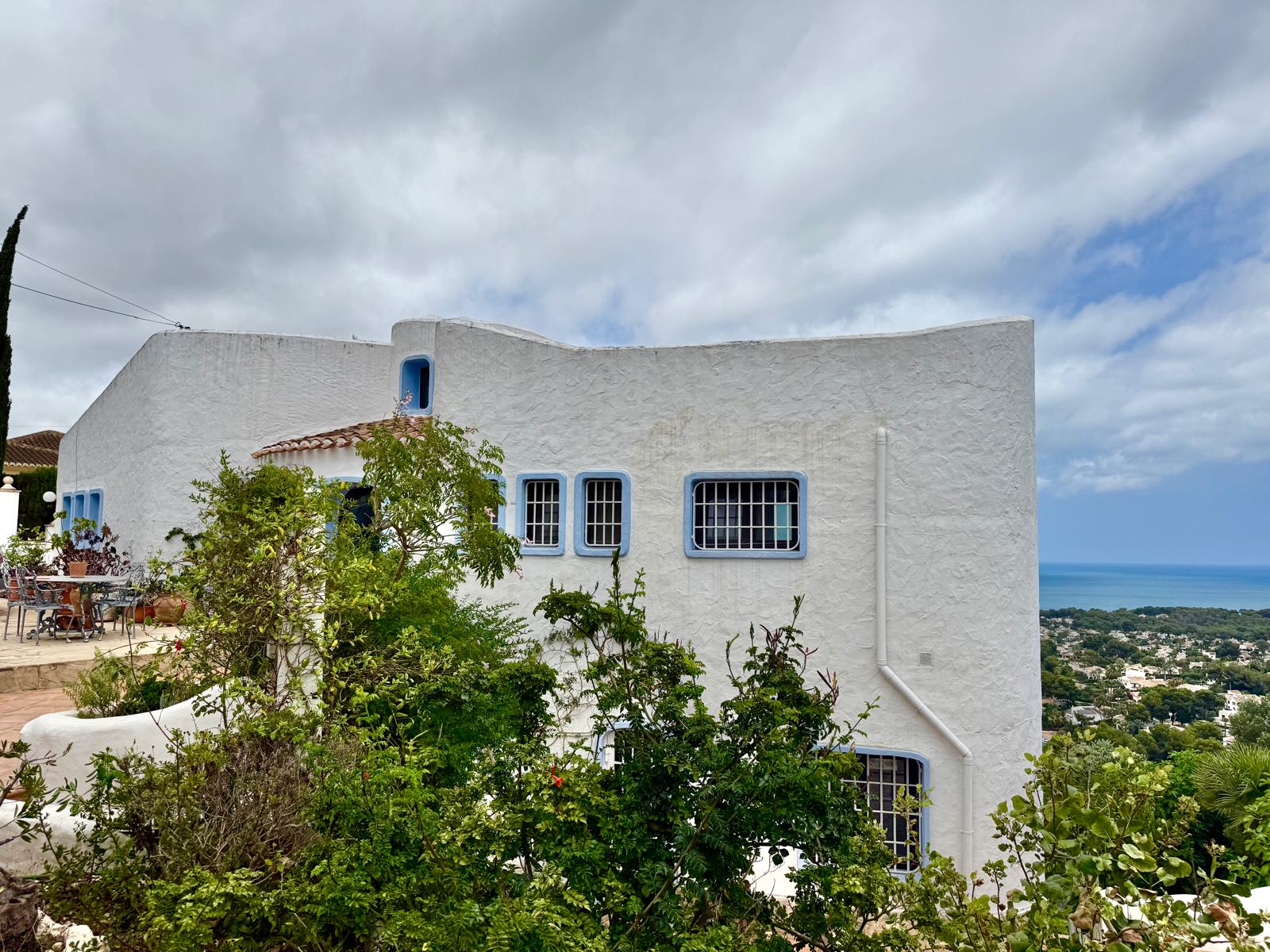 Witte gevel in Ibizastijl met blauw omrande ramen en organische vormen, met een panoramisch uitzicht over de Middellandse Zee.