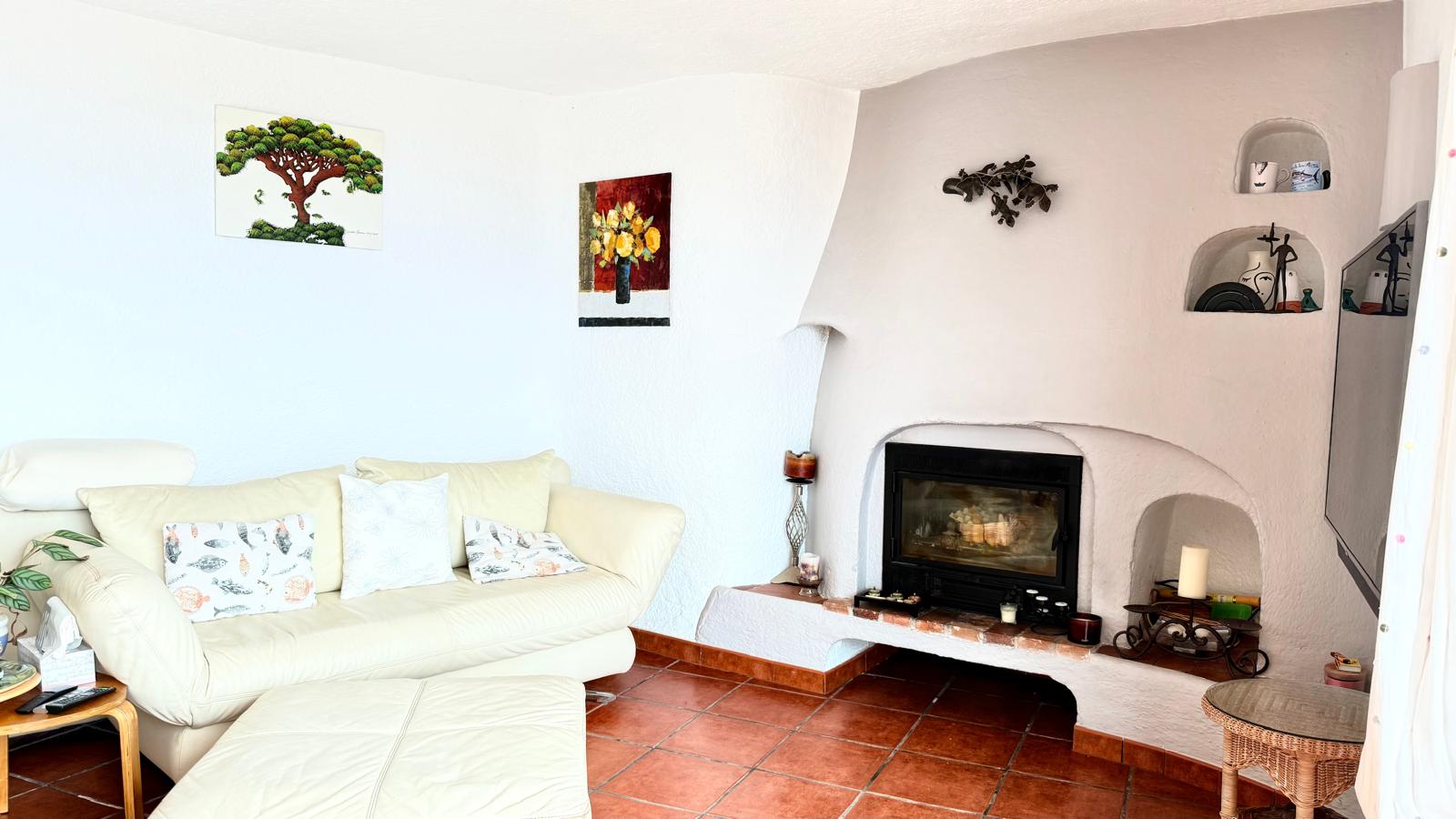 Woonkamer in Ibiza-stijl met een ingebouwde haard, decoratieve nissen in de muur, een authentieke terracotta vloer en witte muren met ronde vormen.
