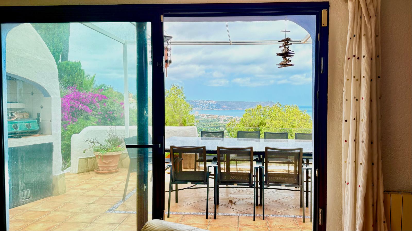 Zicht vanuit de woning op het hoofdterras met een eethoek, ingebouwde barbecue en een panoramisch uitzicht over de baai van Jávea en de Middellandse Zee.