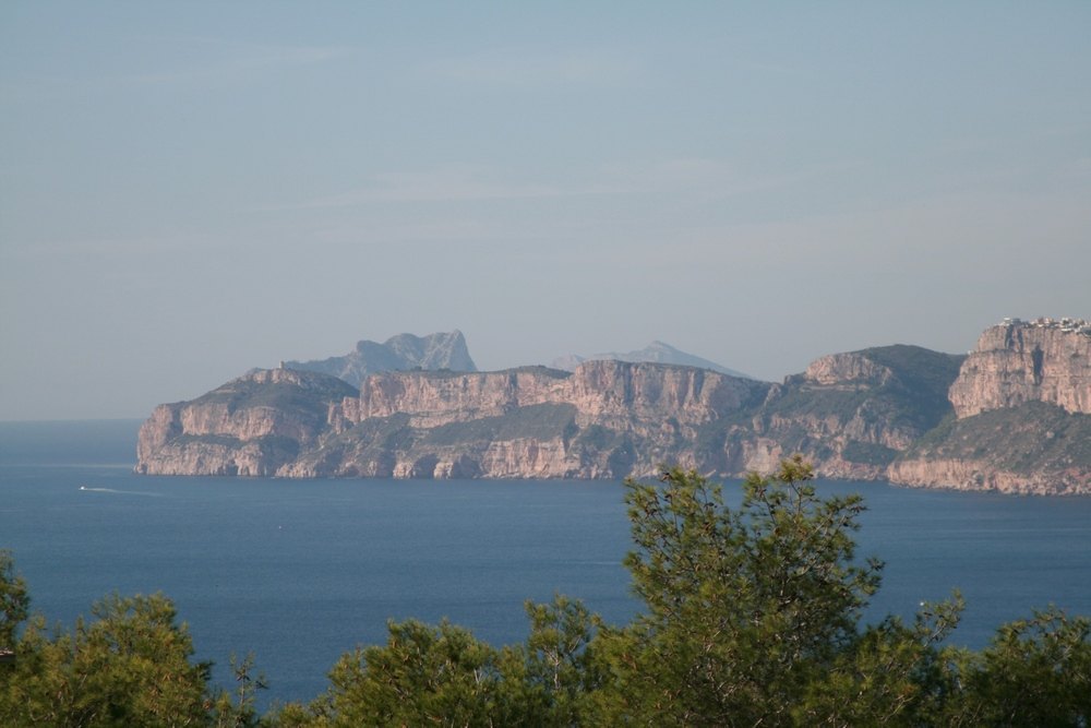 Panoramisch uitzicht op de Middellandse Zee en de kalkrotsen van de kust van Jávea, omgeven door pijnbomen vanaf het perceel.