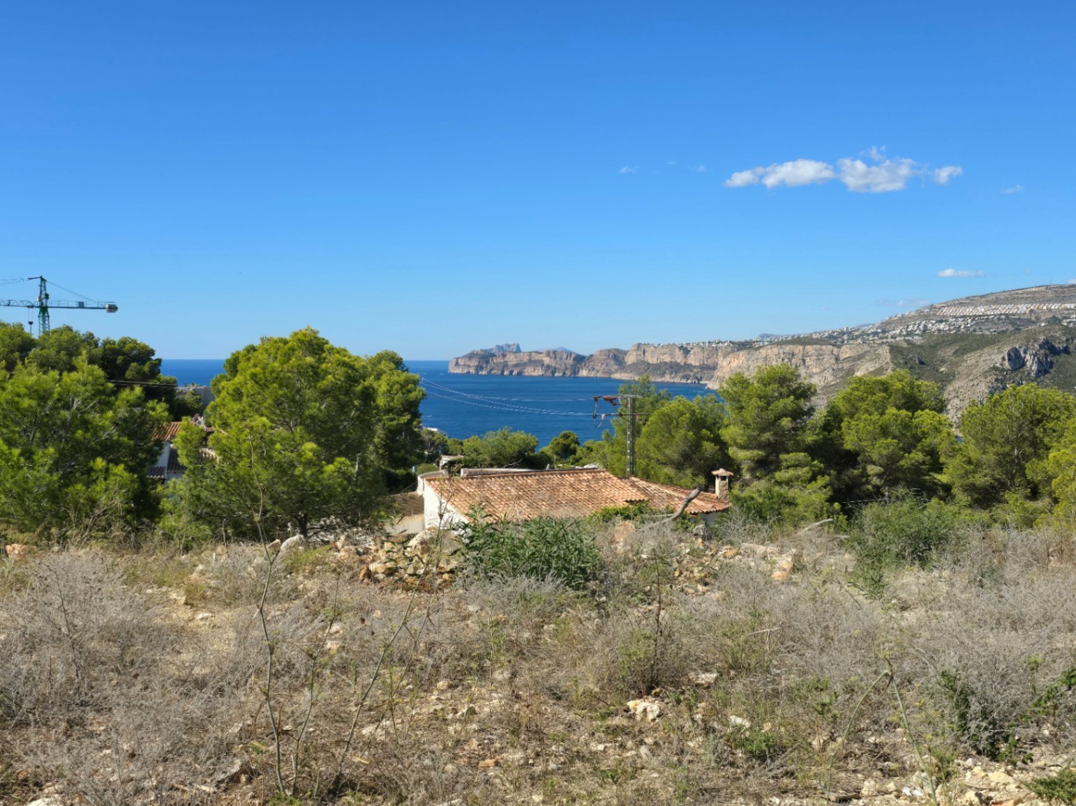 Panoramisch uitzicht op de Middellandse Zee en de kustkliffen vanaf het verhoogde perceel, omgeven door pijnbomen en lokale vegetatie in Jávea.
