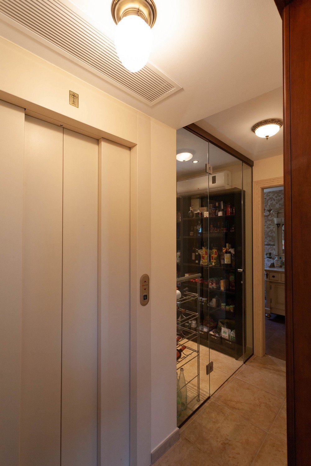 Detail van de interieur lift naast een glazen voorraadkast met metalen rekken.