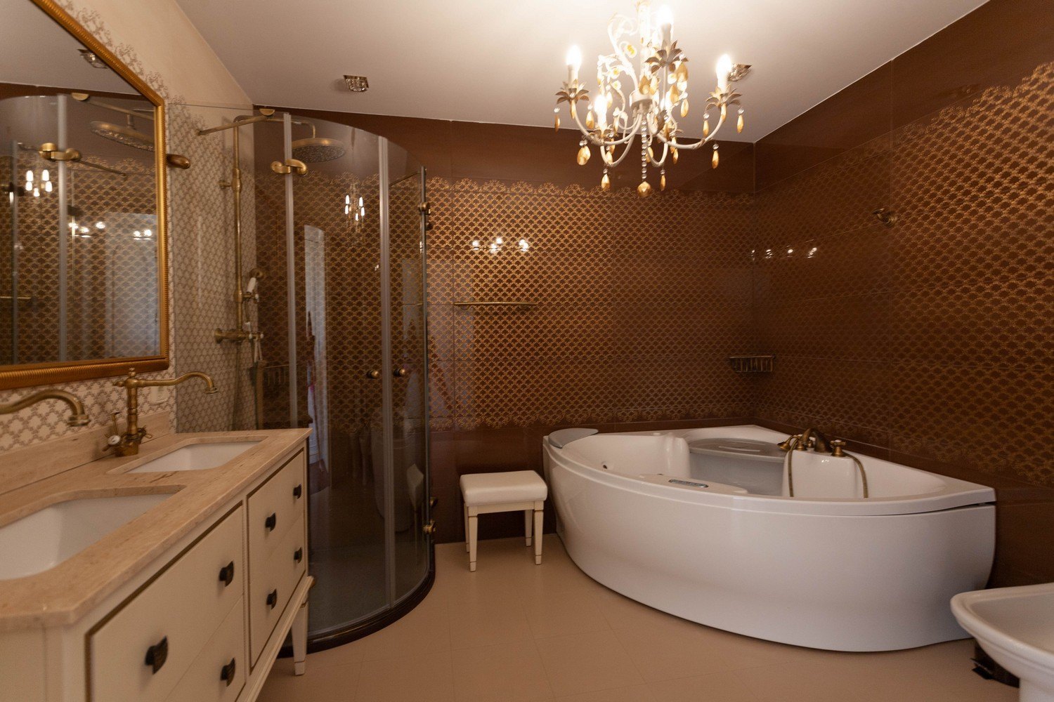 Elegante badkamer met bubbelbad, gebogen glazen douche en dubbele wastafel met gouden armaturen.
