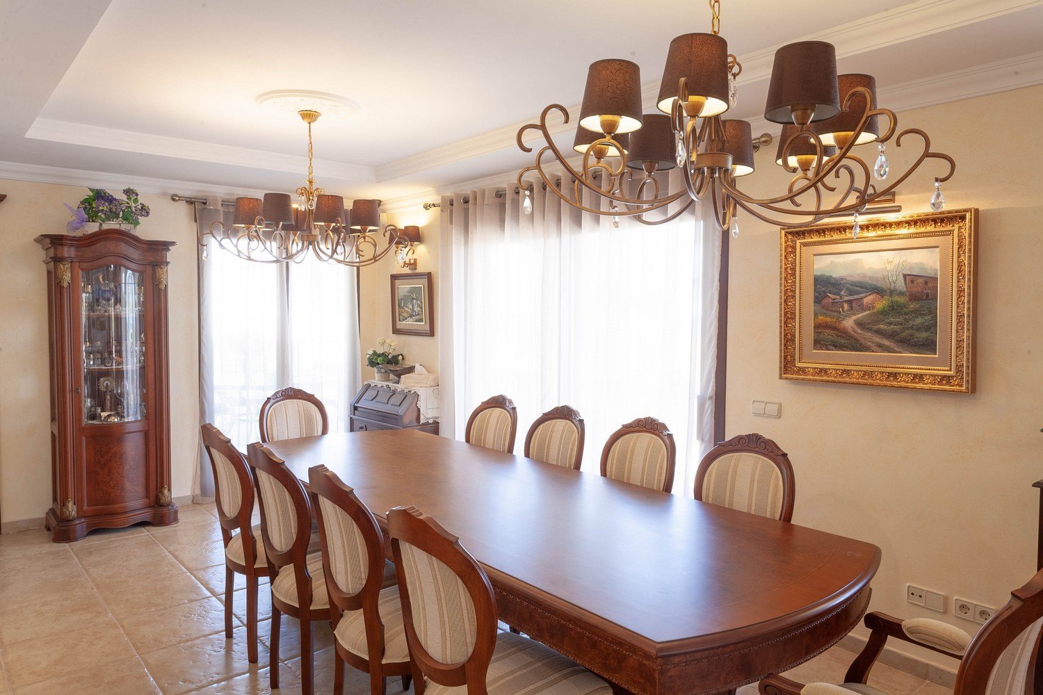 Klassieke eetkamer met houten tafel, gestoffeerde stoelen en antieke vitrinekast. Warme verlichting met kroonluchters.