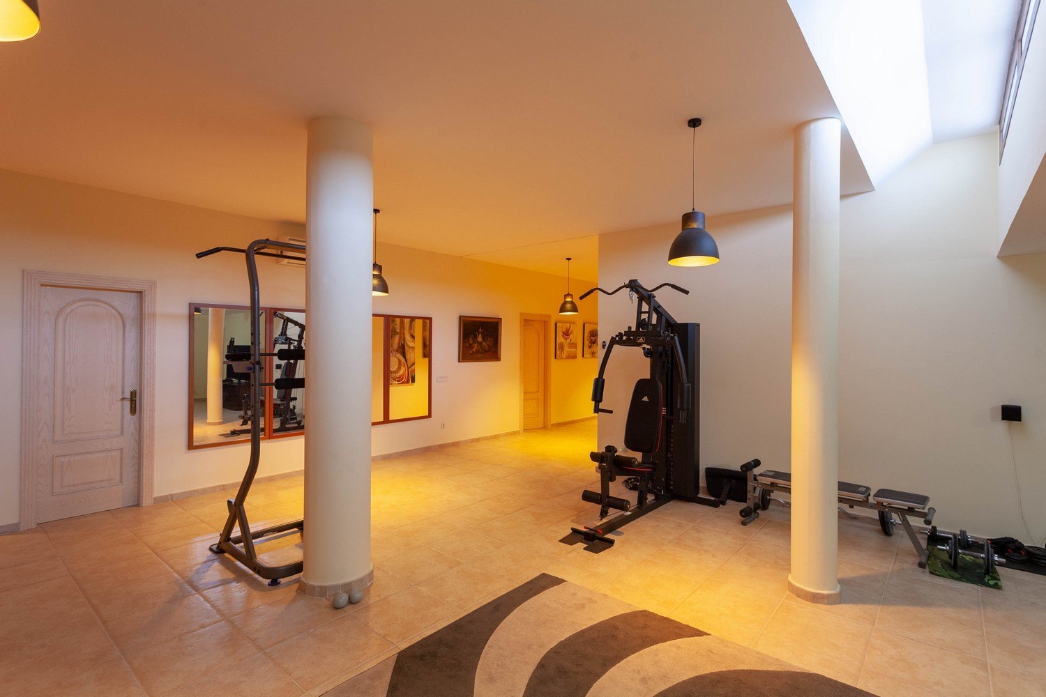 Lichte fitnessruimte met tegelvloer, uitgerust met fitnessapparaten en bovenlicht.