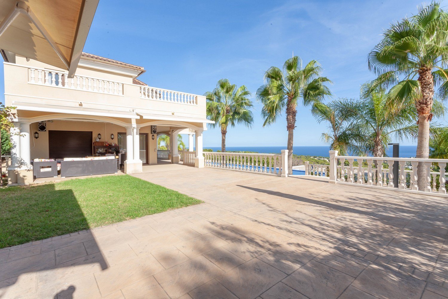 Ruim terras met uitzicht op zee en zwembad, geaccentueerd door palmbomen en een klassieke balustrade.