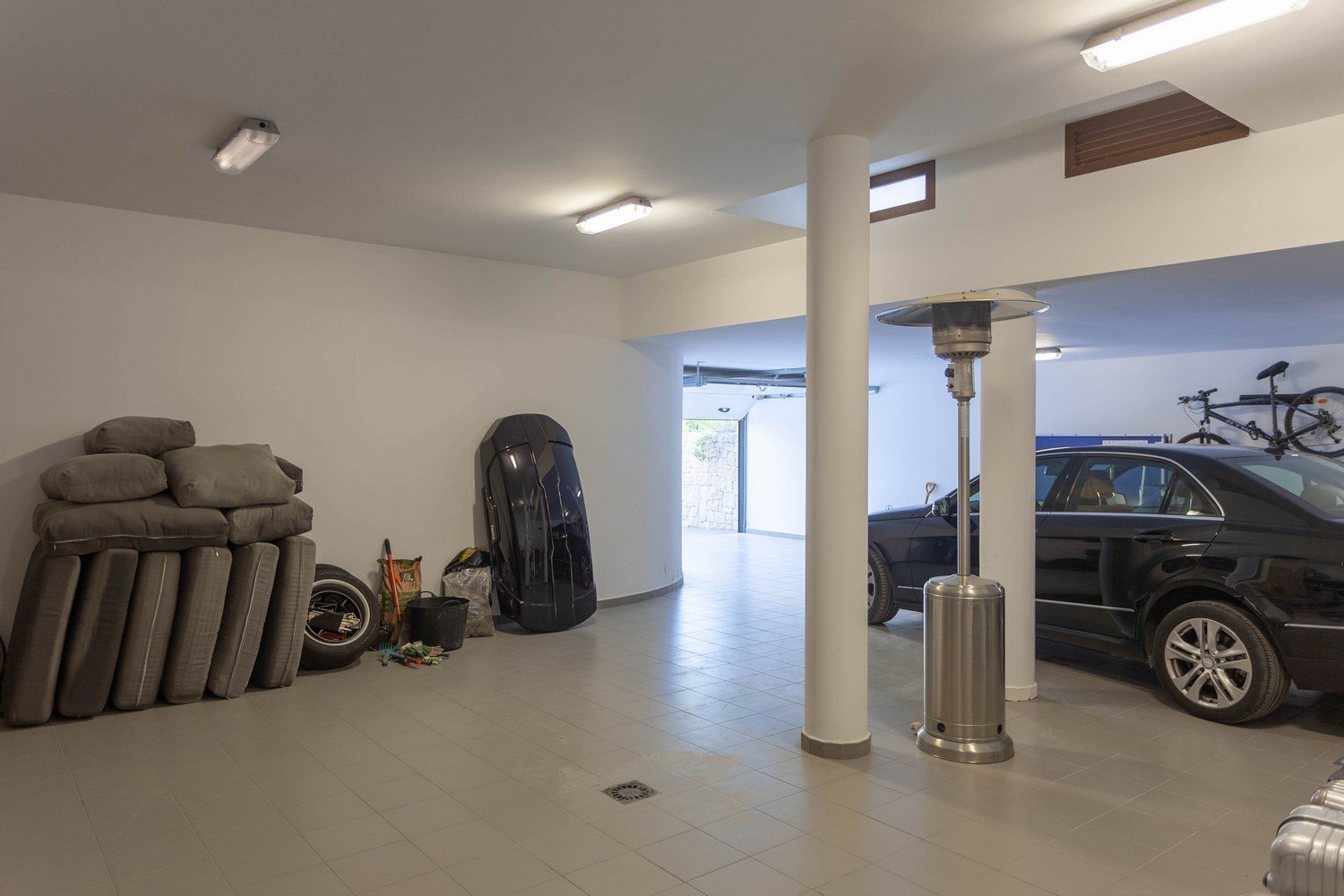 Ruime garage met tegelvloer, zwarte auto en diverse opgeslagen accessoires.