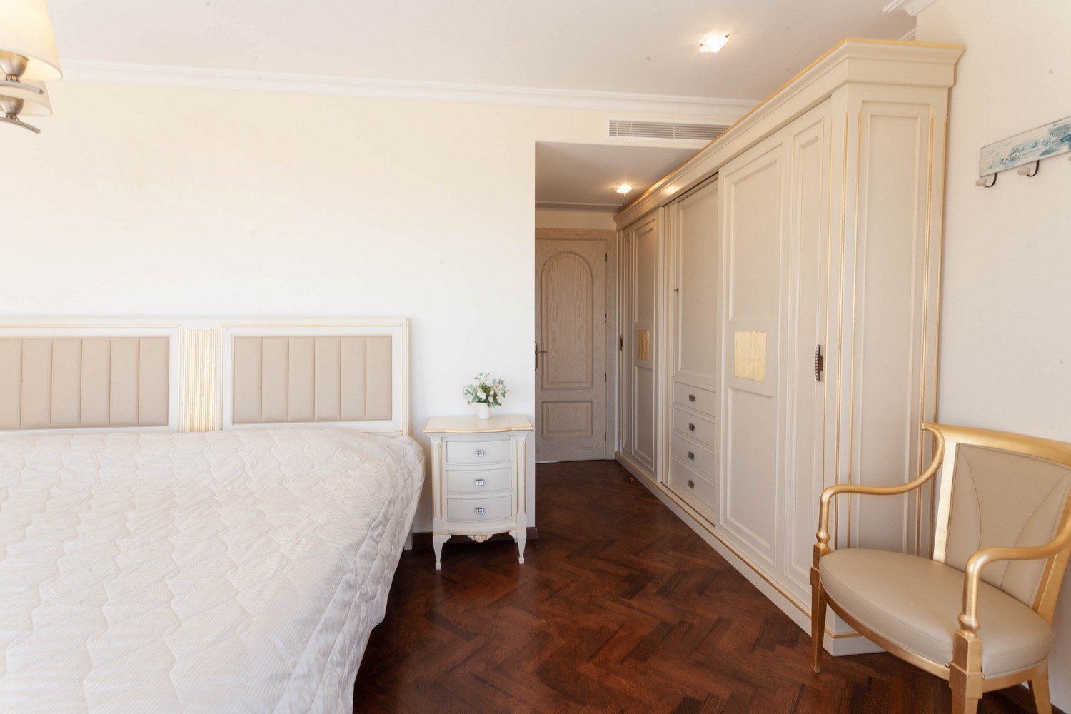 Slaapkamer met bed met gestoffeerd hoofdeinde, licht houten inbouwkast en donkere parketvloer.