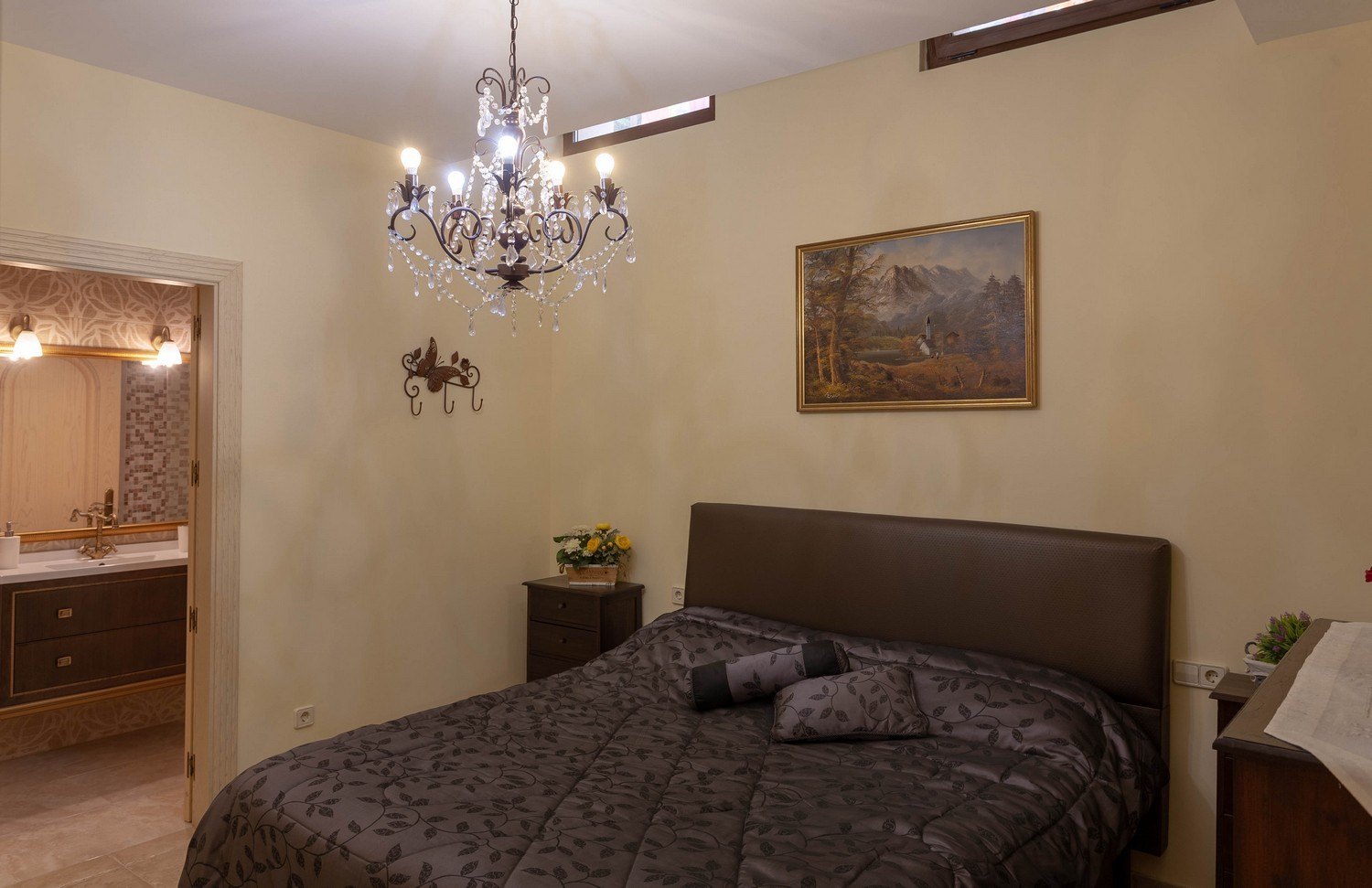 Slaapkamer met tweepersoonsbed, kristallen kroonluchter en toegang tot een en-suite badkamer met dubbele wastafel.