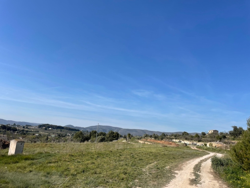 Uitzicht op het land met een zandweg en een bergachtige horizon onder een helderblauwe hemel.