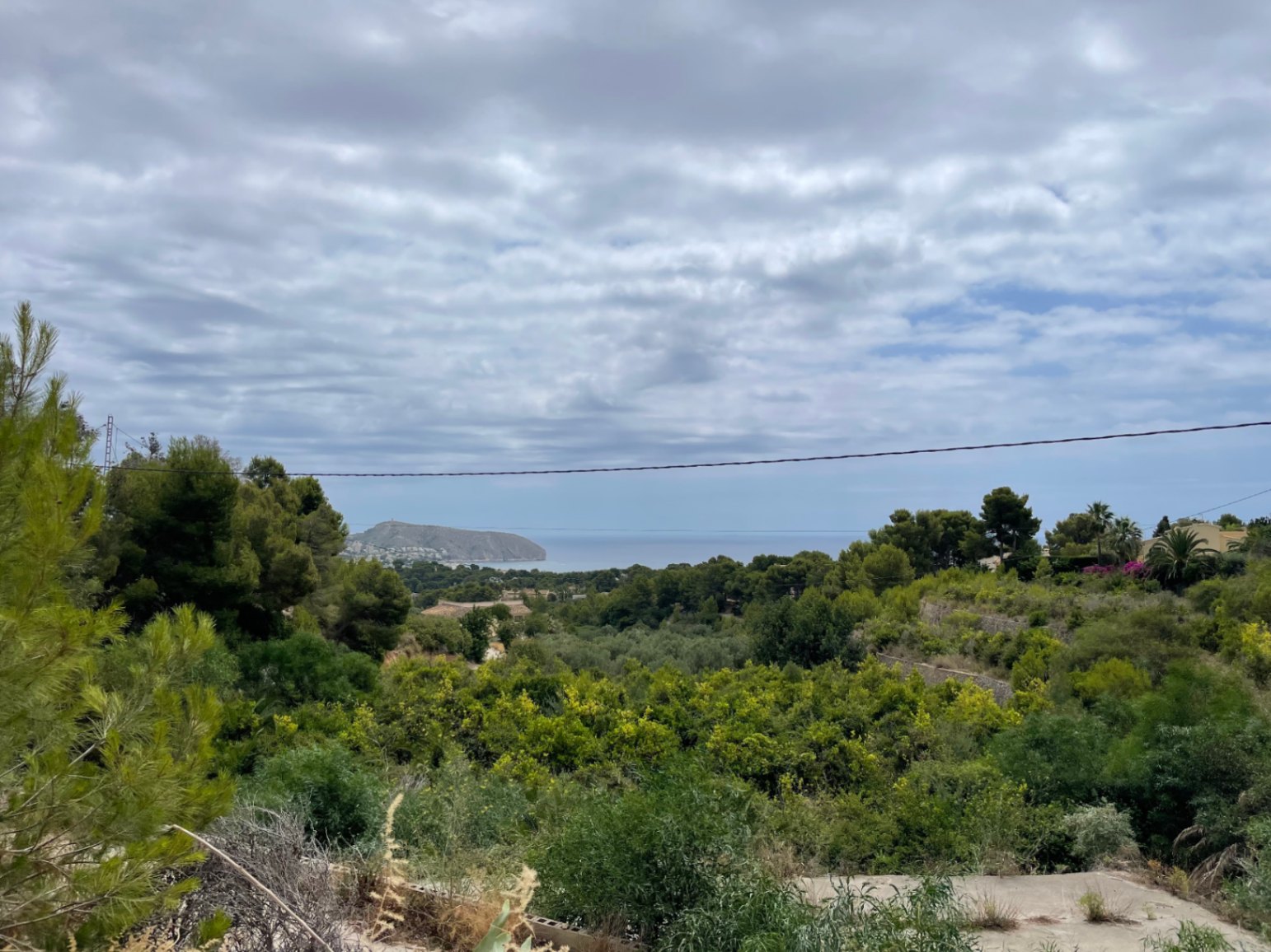 Panoramisch uitzicht op de Middellandse Zee en de kustlijn vanaf het hooggelegen perceel, omgeven door pijnbomen en weelderige mediterrane begroeiing.