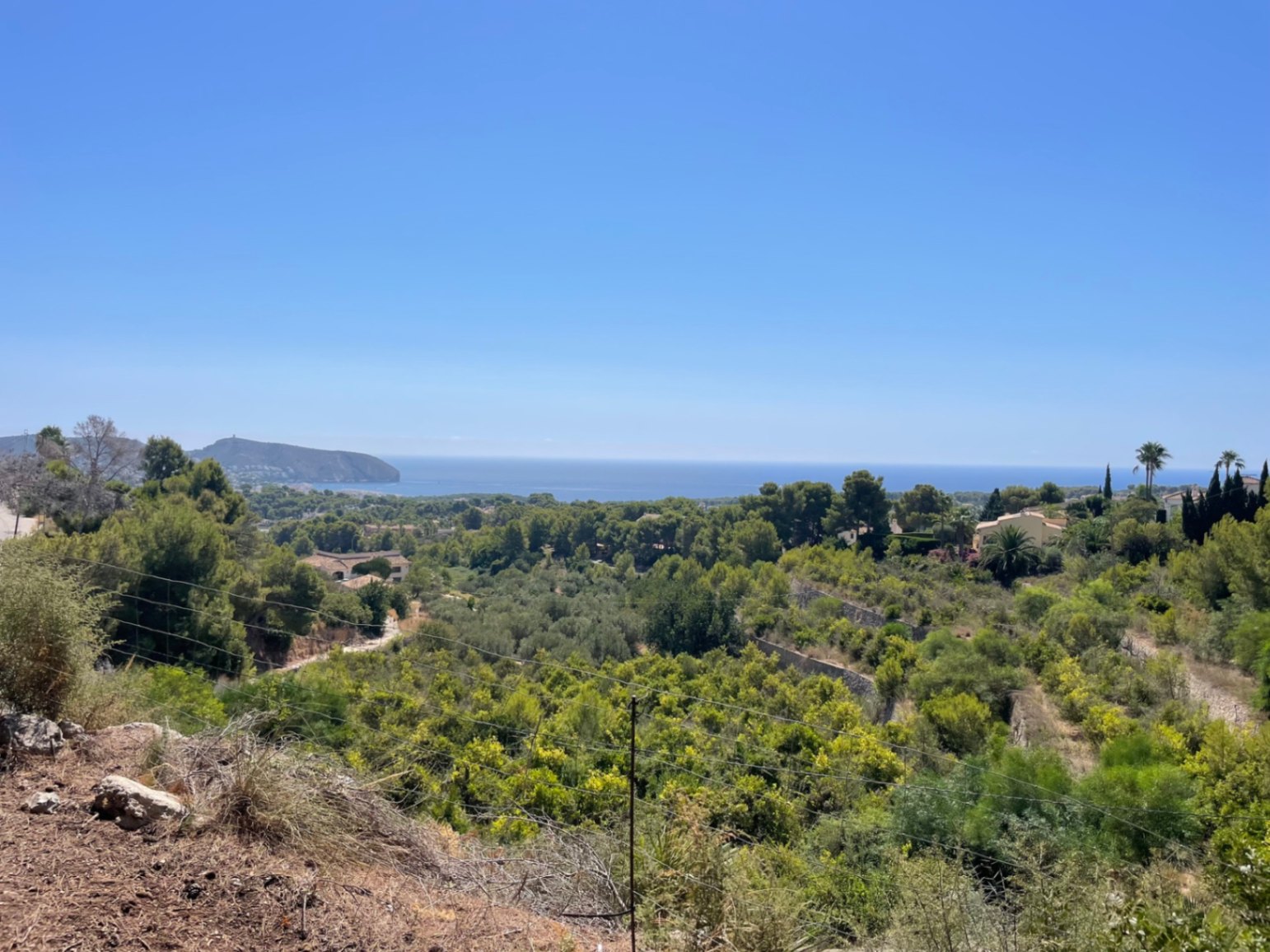 Panoramisch uitzicht vanaf het perceel op de Middellandse Zee en Cap d'Or, omgeven door een groene vallei met pijnbomen en lokale vegetatie in Moraira.