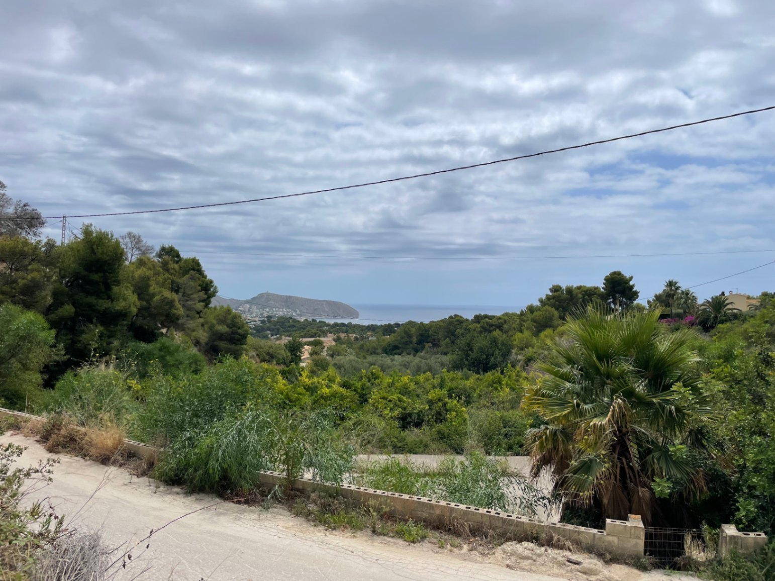 Verhoogd panoramisch uitzicht op de Middellandse Zee en de kustlijn van Moraira, omgeven door inheemse pijnbomen en weelderige vegetatie.
