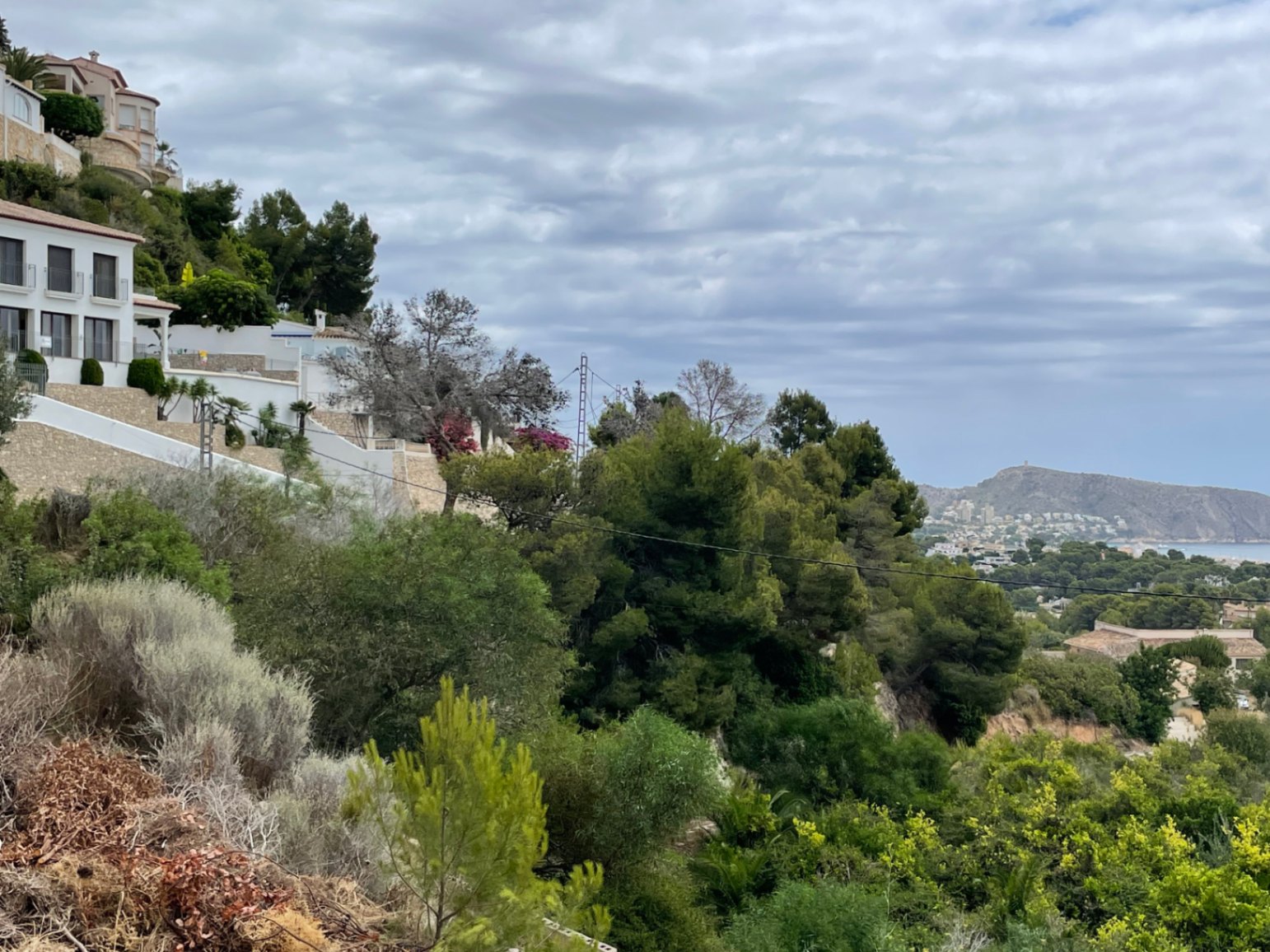 Verhoogd uitzicht vanaf de heuvel van Benimeit met mediterrane begroeiing, villa's met natuurstenen muren en een weids panorama over de kustlijn.
