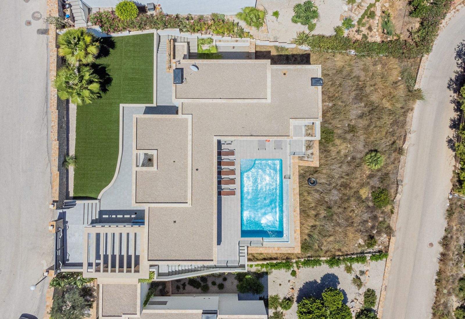 Bovenaanzicht van de moderne villa met het rechthoekige zwembad, zonneterras met ligbedden en de aangelegde tuin met kunstgras.