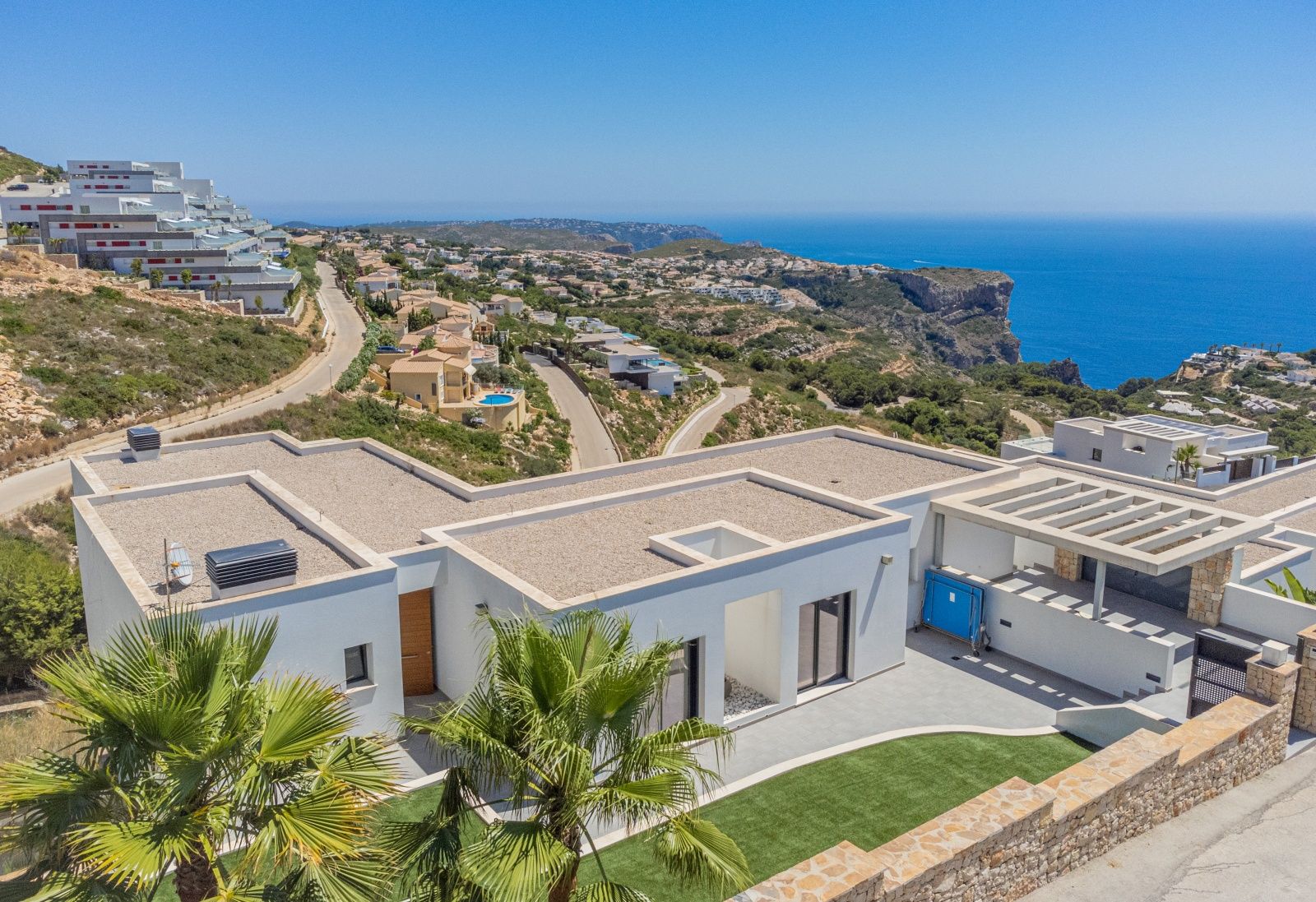 Luchtfoto van de moderne villa in Cumbre del Sol, met platte daken, witte gevels en panoramisch uitzicht op de Middellandse Zee en de kustkliffen.