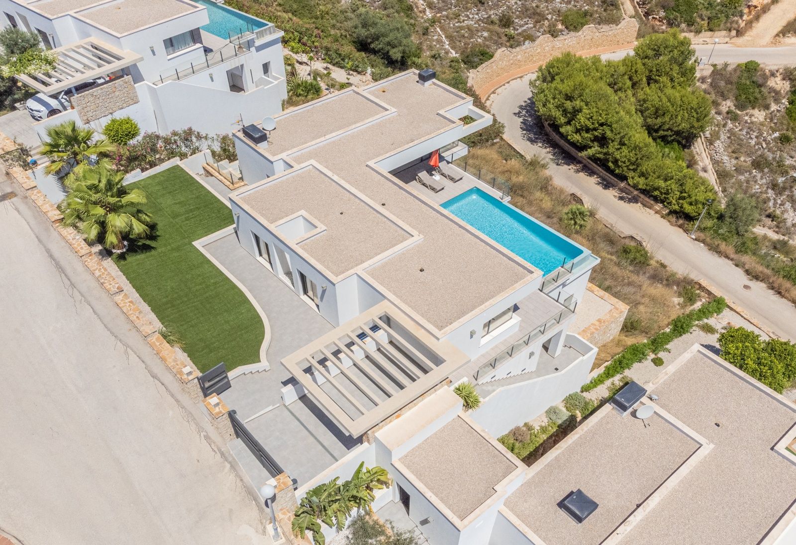 Luchtfoto van de moderne villa met strakke architectuur, een overloopzwembad, platte grinddaken en een tuin met kunstgras.
