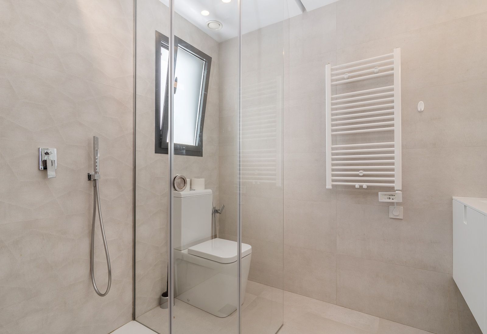 Moderne badkamer met glazen inloopdouche, beige getextureerde wandtegels, een witte handdoekradiator en inbouwspots in het plafond.