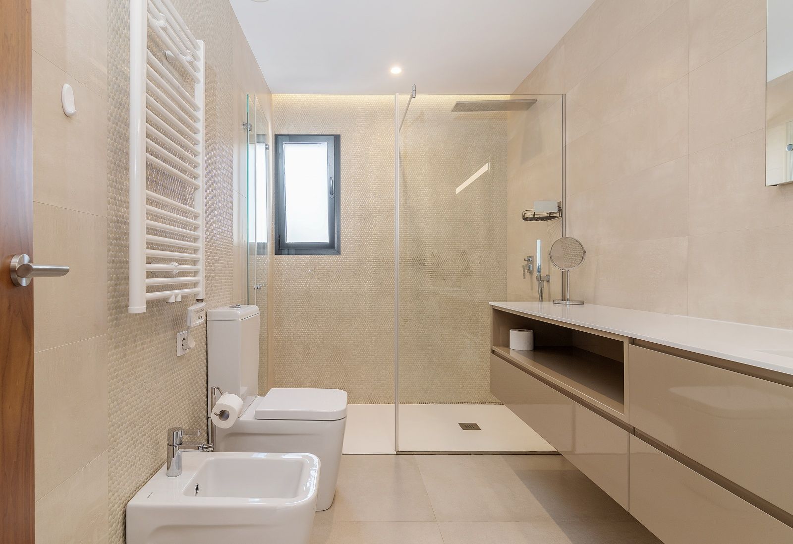 Moderne badkamer met inloopdouche, glazen wand, zwevend wastafelmeubel, bidet en witte handdoekradiator, uitgevoerd in neutrale tinten.
