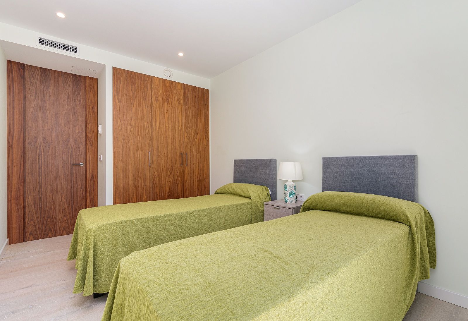 Moderne slaapkamer met twee eenpersoonsbedden, ingebouwde kasten van natuurlijk hout, airconditioning via kanalen en inbouwspots.