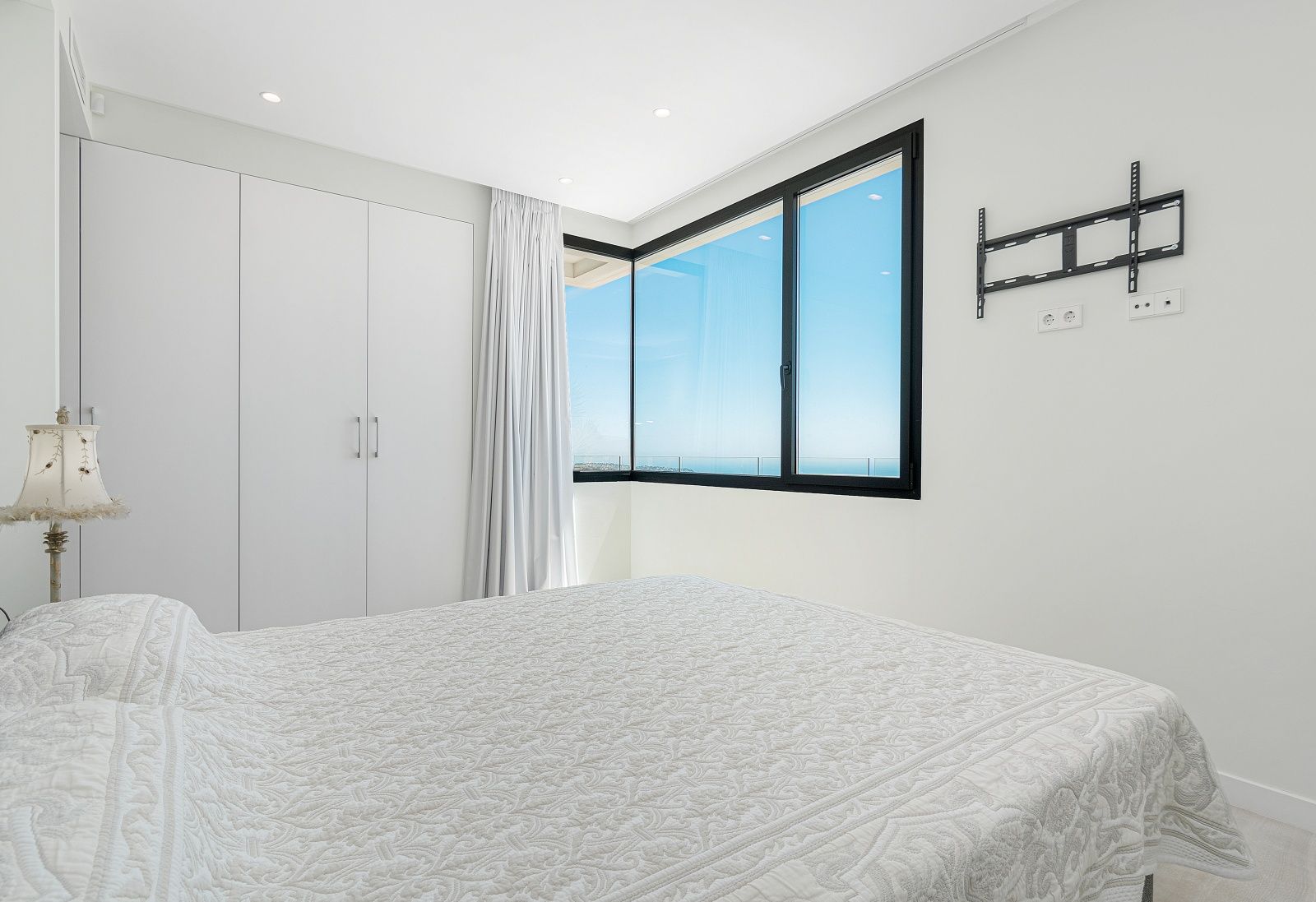 Moderne slaapkamer met witte inbouwkasten, een hoekvenster met zwarte kozijnen en panoramisch uitzicht op de Middellandse Zee.