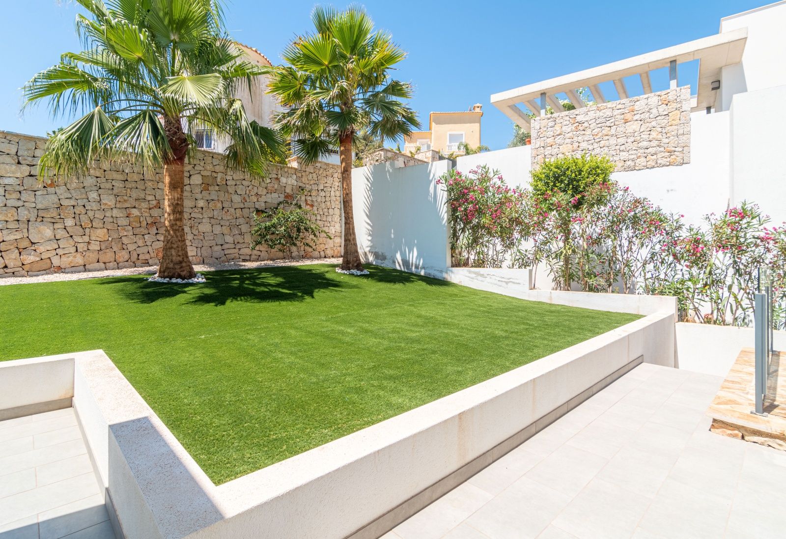 Onderhoudsvriendelijke designtuin met kunstgras, palmbomen en natuurstenen muren, geïntegreerd in de moderne architectuur van de villa.