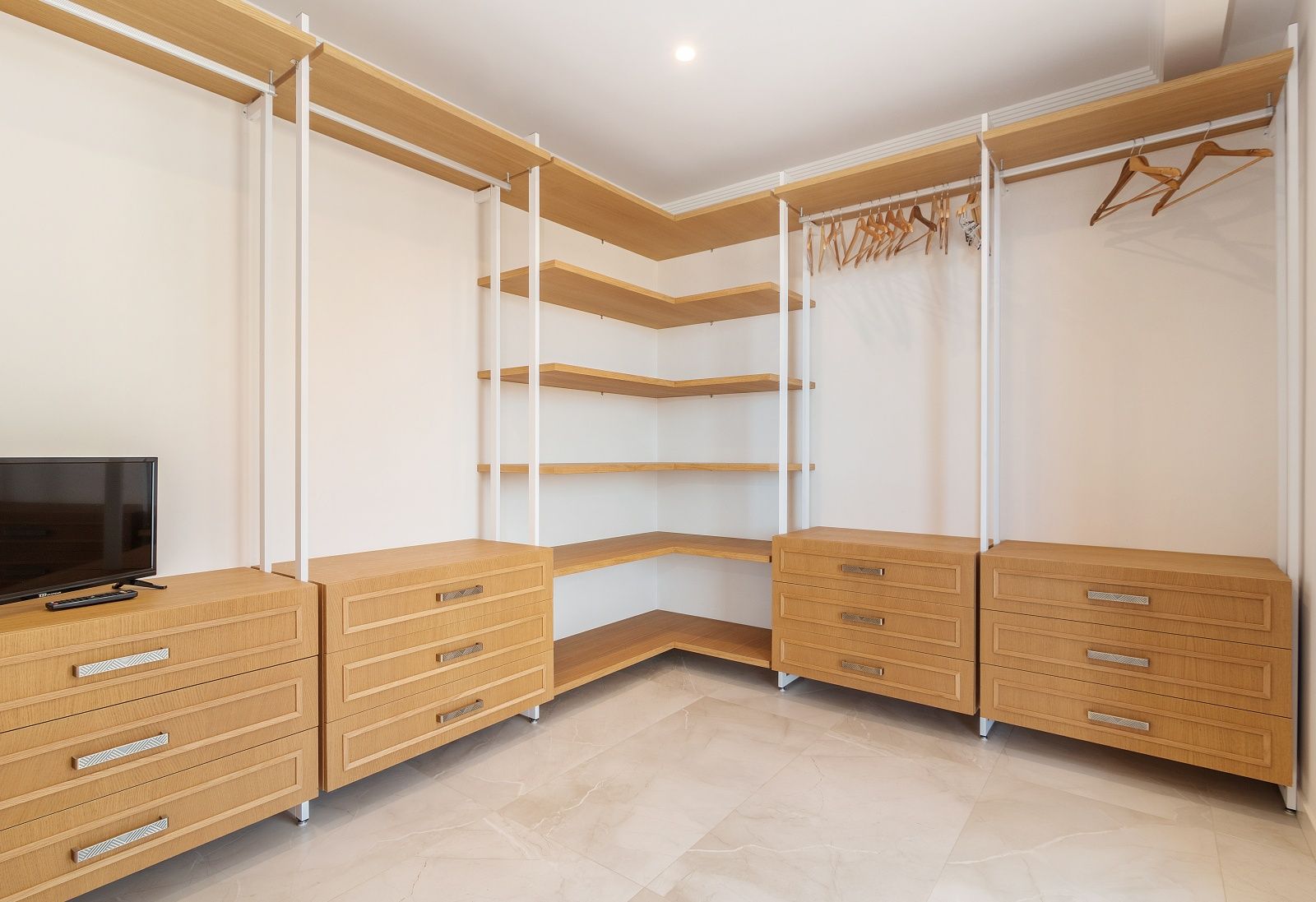 Open inloopkast met eikenhouten planken, modulaire ladekasten en een gepolijste porseleinen vloer met marmerlook.